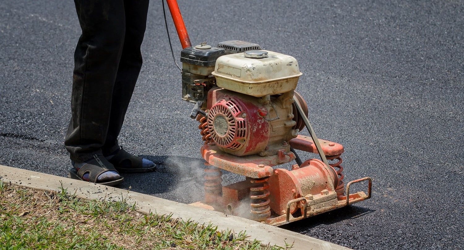 Worker uses vibratory plate compactor compacting asphalt at road repair