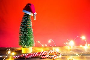 Christmas tree on a red background with lights of garlands, caramel striped cane, Santa hat, tinsel. New year, festive atmosphere. Copy space