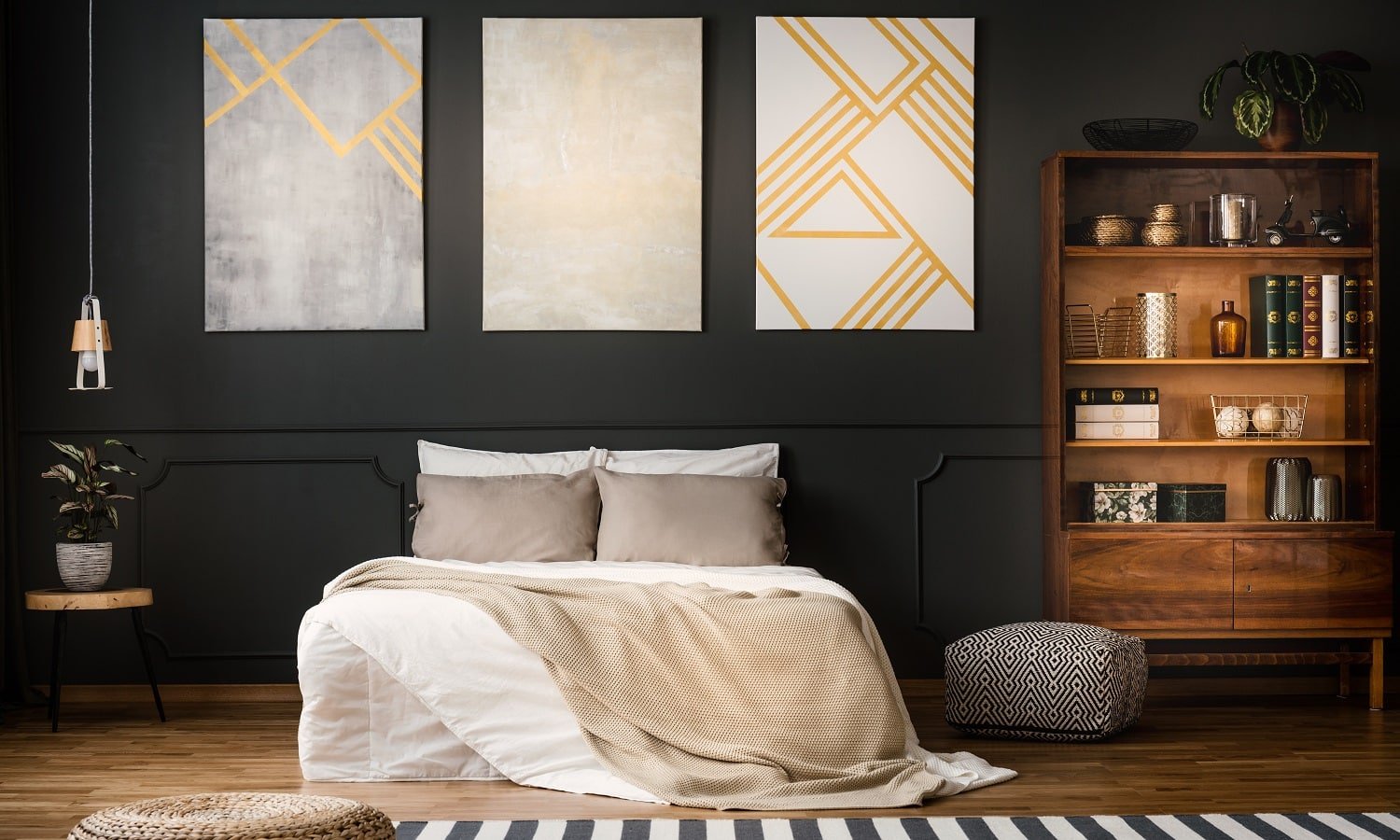 Elegant, wooden, antique bookcase in a dark, modern bedroom interior with a black wall and beige paintings with golden elements