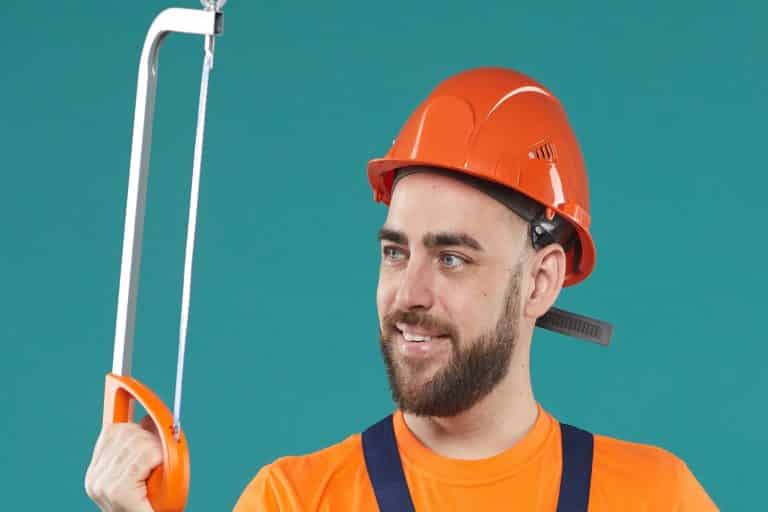 Horizontal medium studio portrait of young adult carpenter holding bow saw standing against turquoise wall background