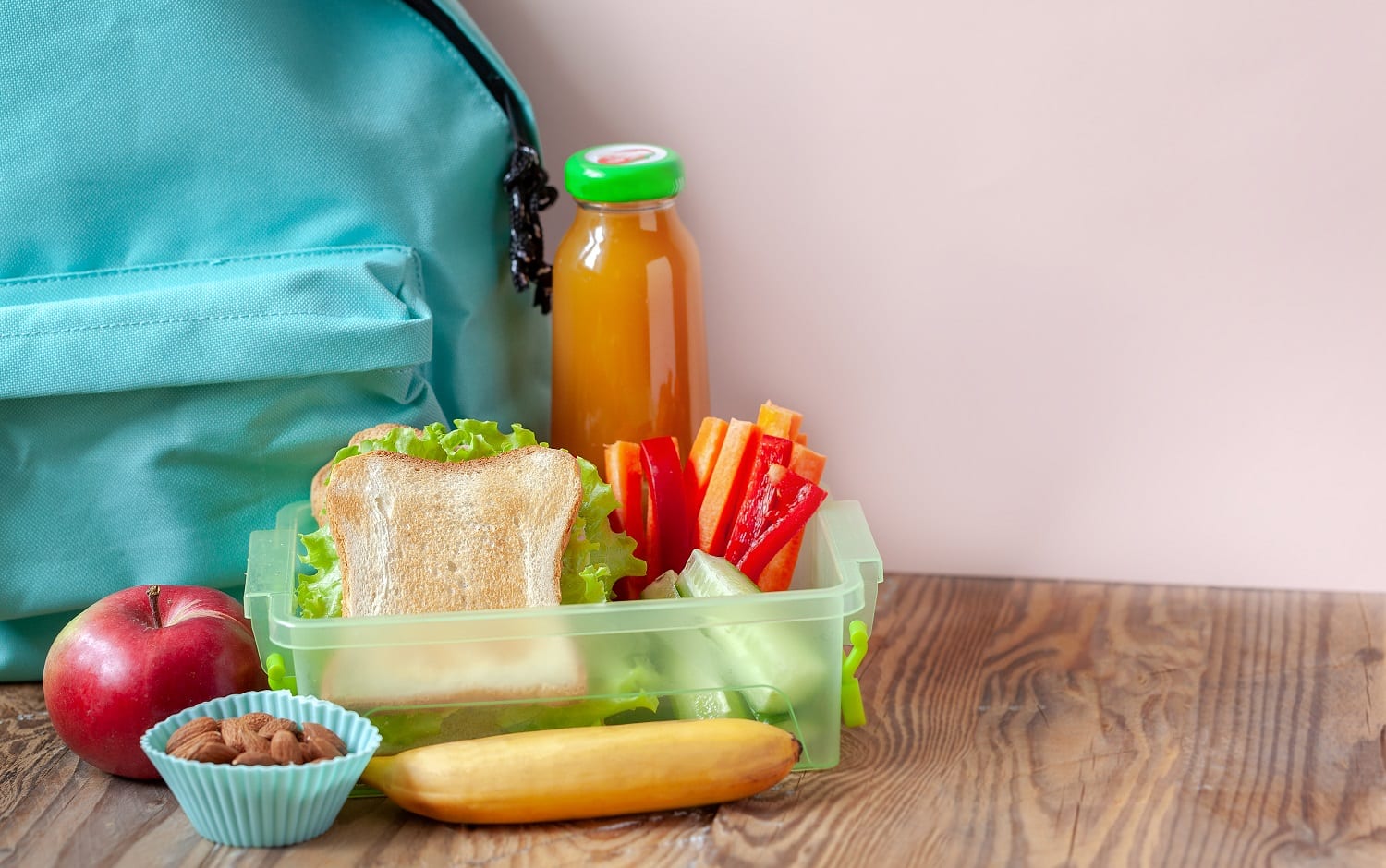 Lunch box with appetizing food and apple, juce, backpack on wooden table
