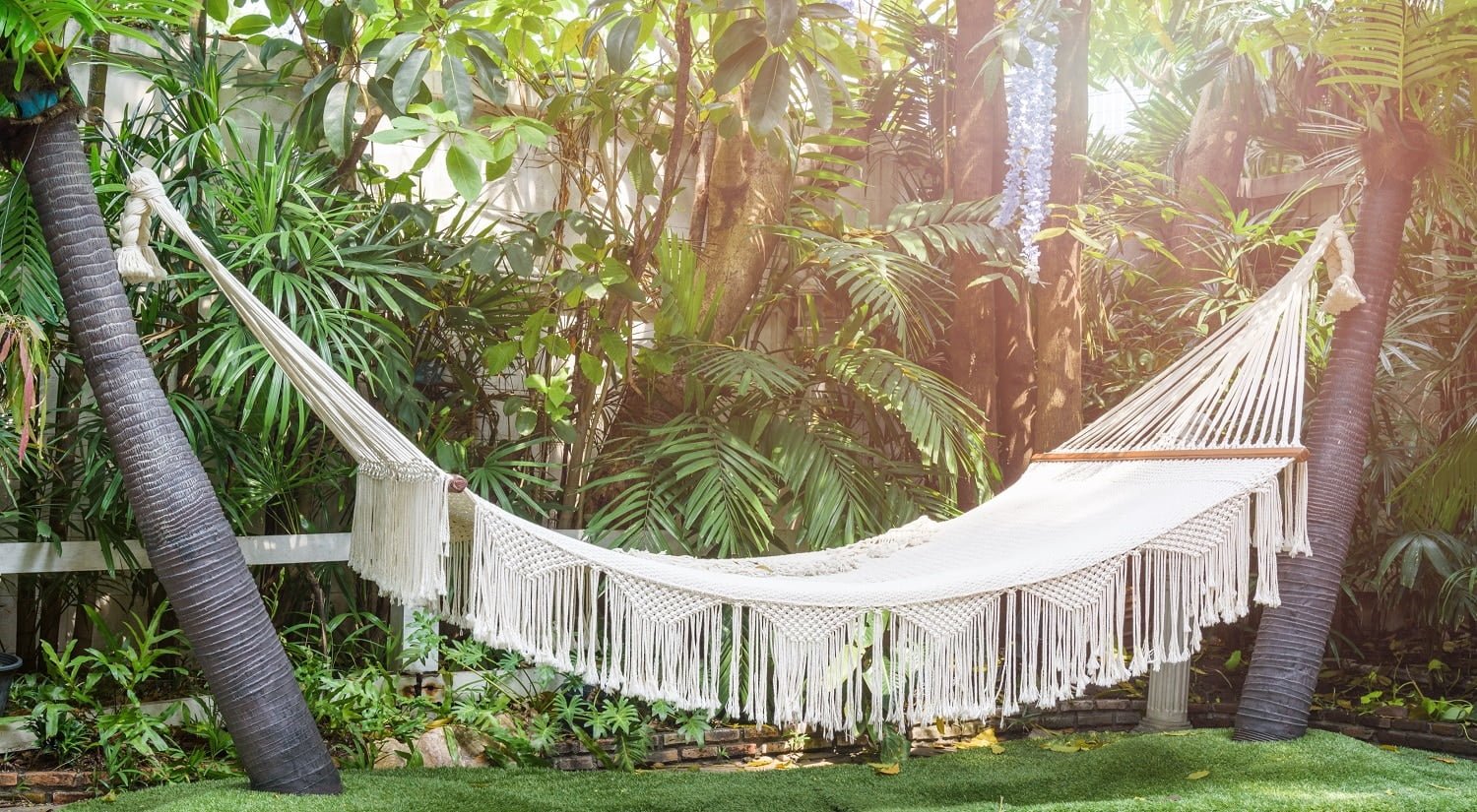 Empty white hammock hanging between palm trees on the garden for recreation or relaxation on summer day