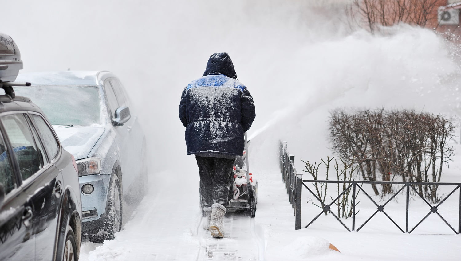 man removes snow in the yard of a multistory building with snow machines