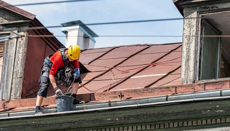 Riga, Latvia- July 3, 2020: Industrial climber removes leaves and dirt from house rooftop rain gutter