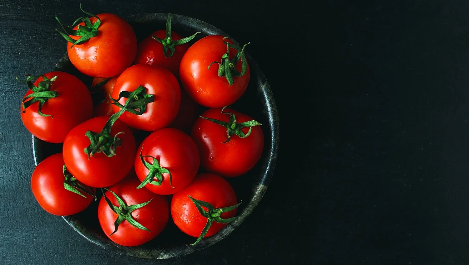 Fresh organic red tomatoes in black plate on black background