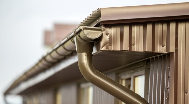 Close-up detail of cottage house corner with metal planks siding and roof with steel gutter rain system. Durability, professional construction, drainage pipes installation and connection concept.