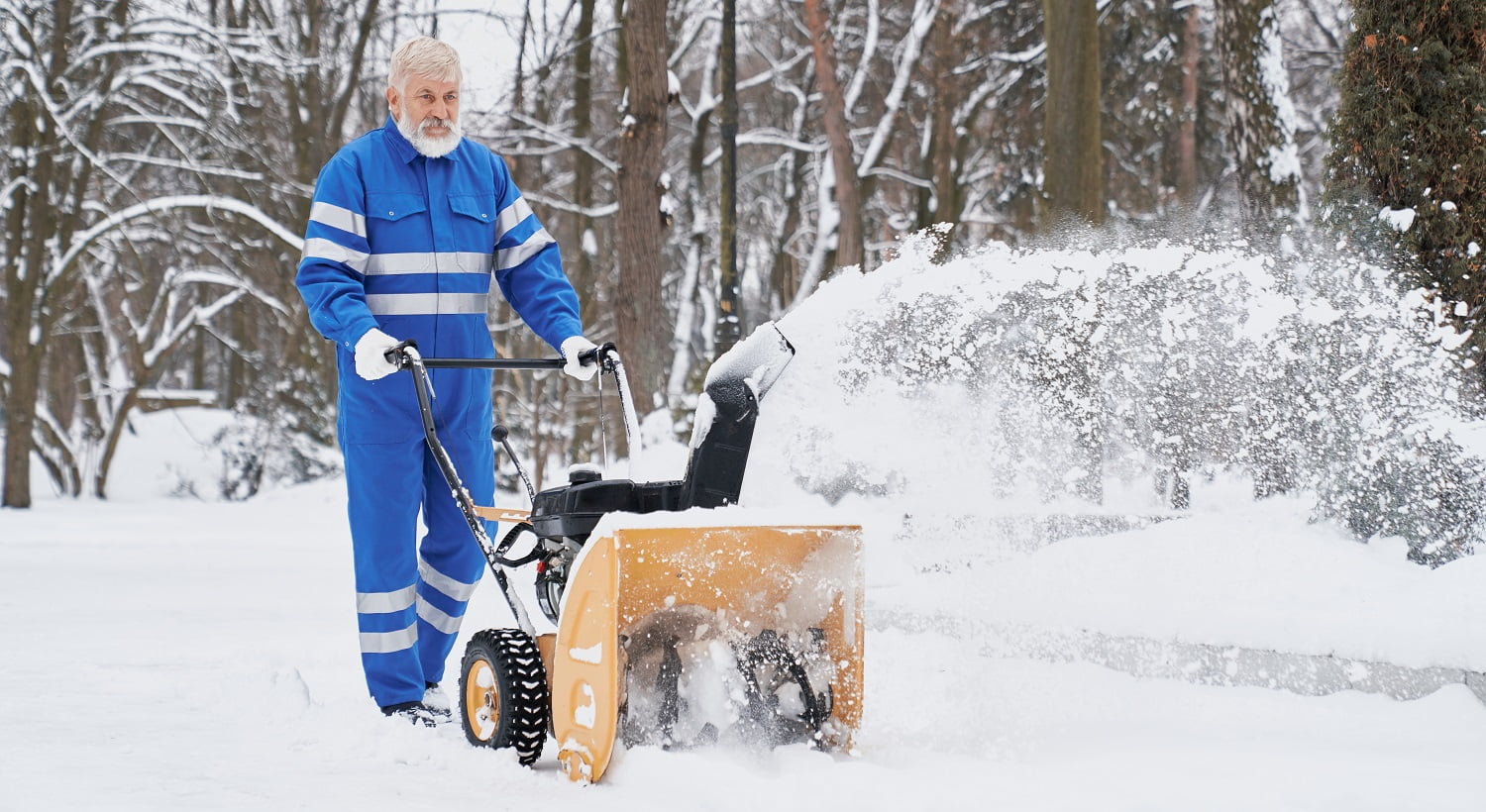 View from side bearded man wearing blue uniform working with snowblower and removing snow from footpath. Elder man keeping machine and driving in park. Concept of city service and maintenance.