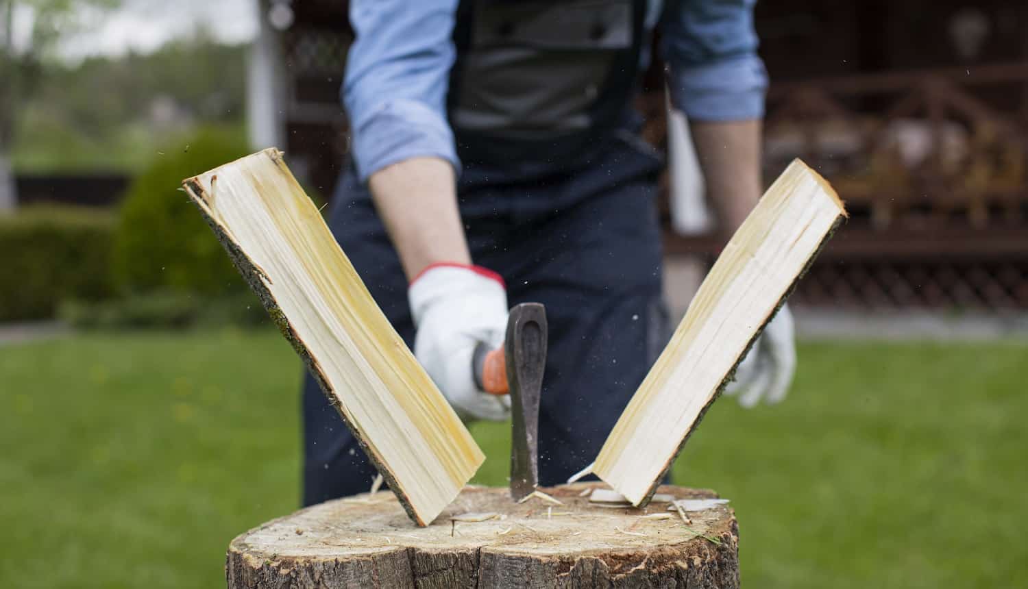 Close up strong man lumberjack in uniform chopping wood with sharp ax on wooden hemp, sawdust fly to sides. Powerful ax blow, woodworking, harvesting wood for winter. Splitting logs with sharp hatchet