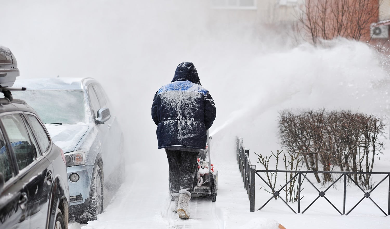 man removes snow in the yard of a multistory building with snow machines