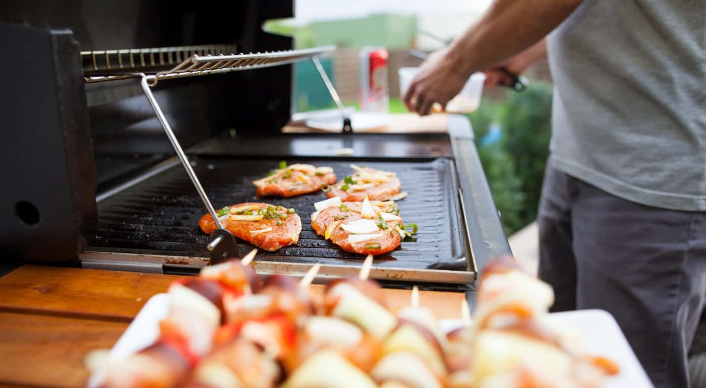Young man grills some kind of marinated meat and vegetable on gas grill during summer time