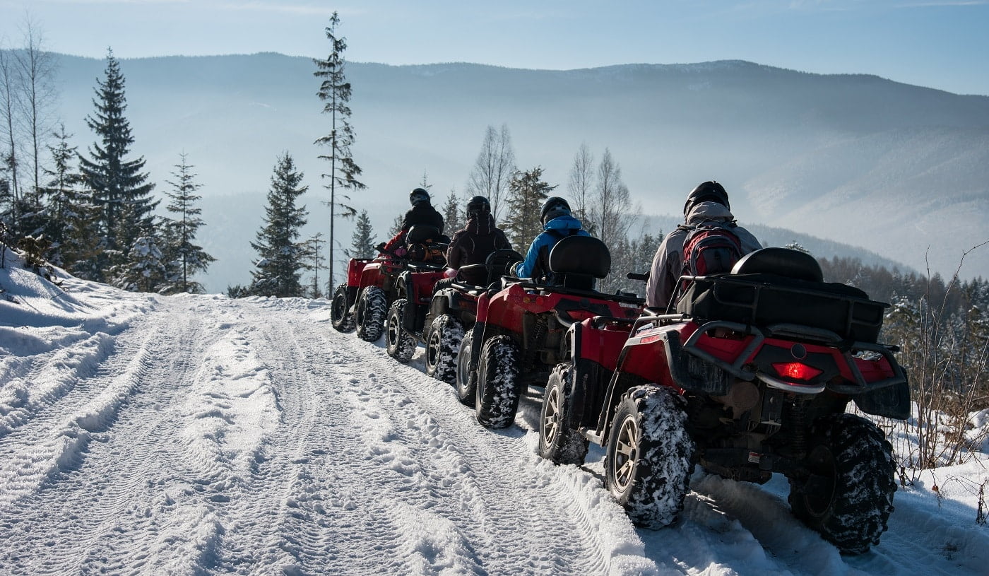 Four ATV riders on off-road quad bikes on snow in the winter mountains