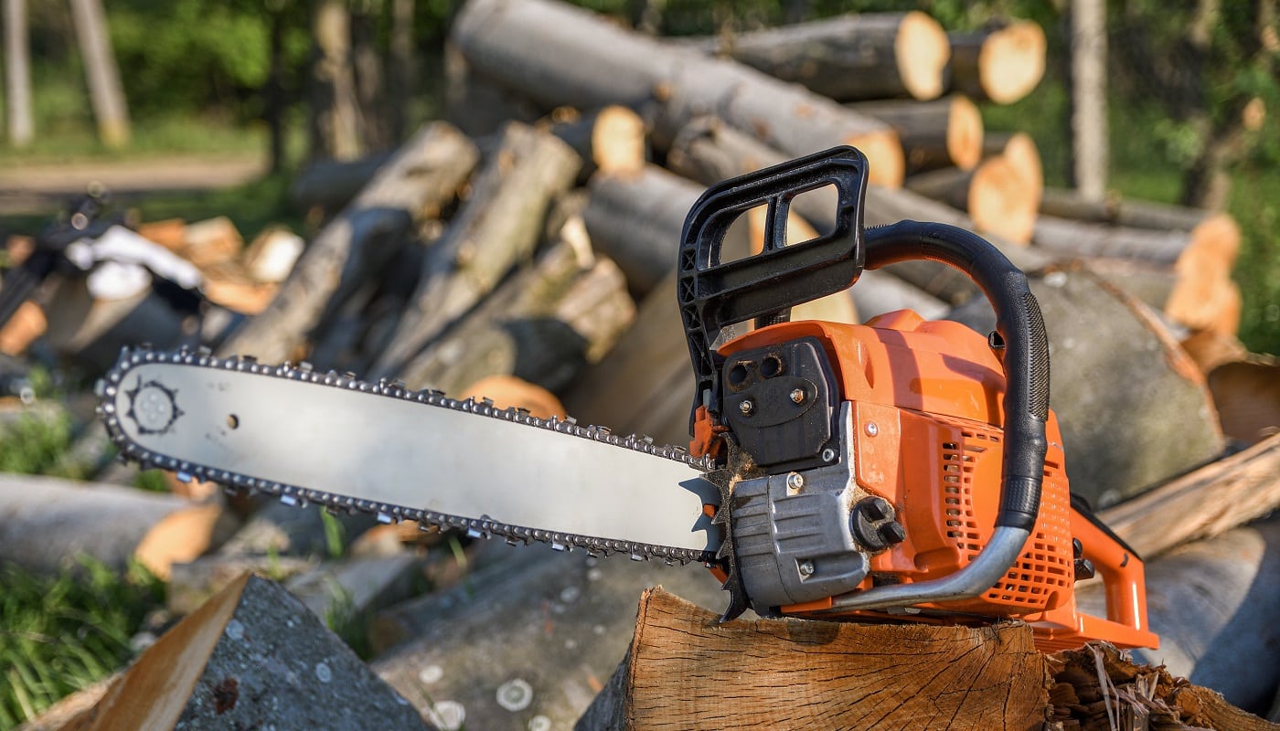 Chainsaw that stands on a heap of firewood in the yard on a background of firewood and trees cut by a chainsaw.