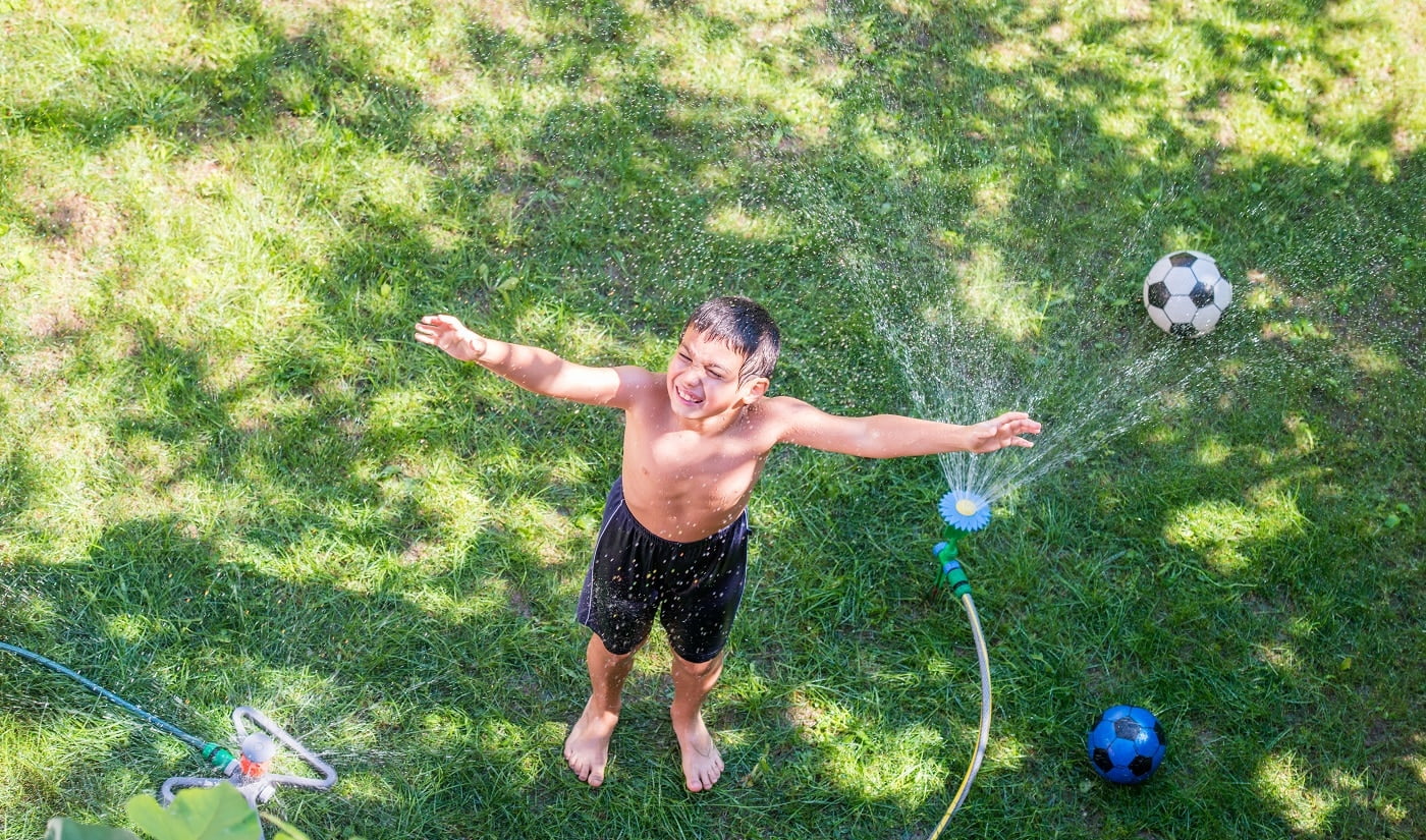 Happy boy playing with water sprinkler for lods