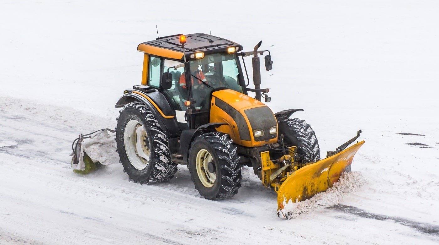 Large snow plowing tractor machine at work on the road during a snow storm in winter