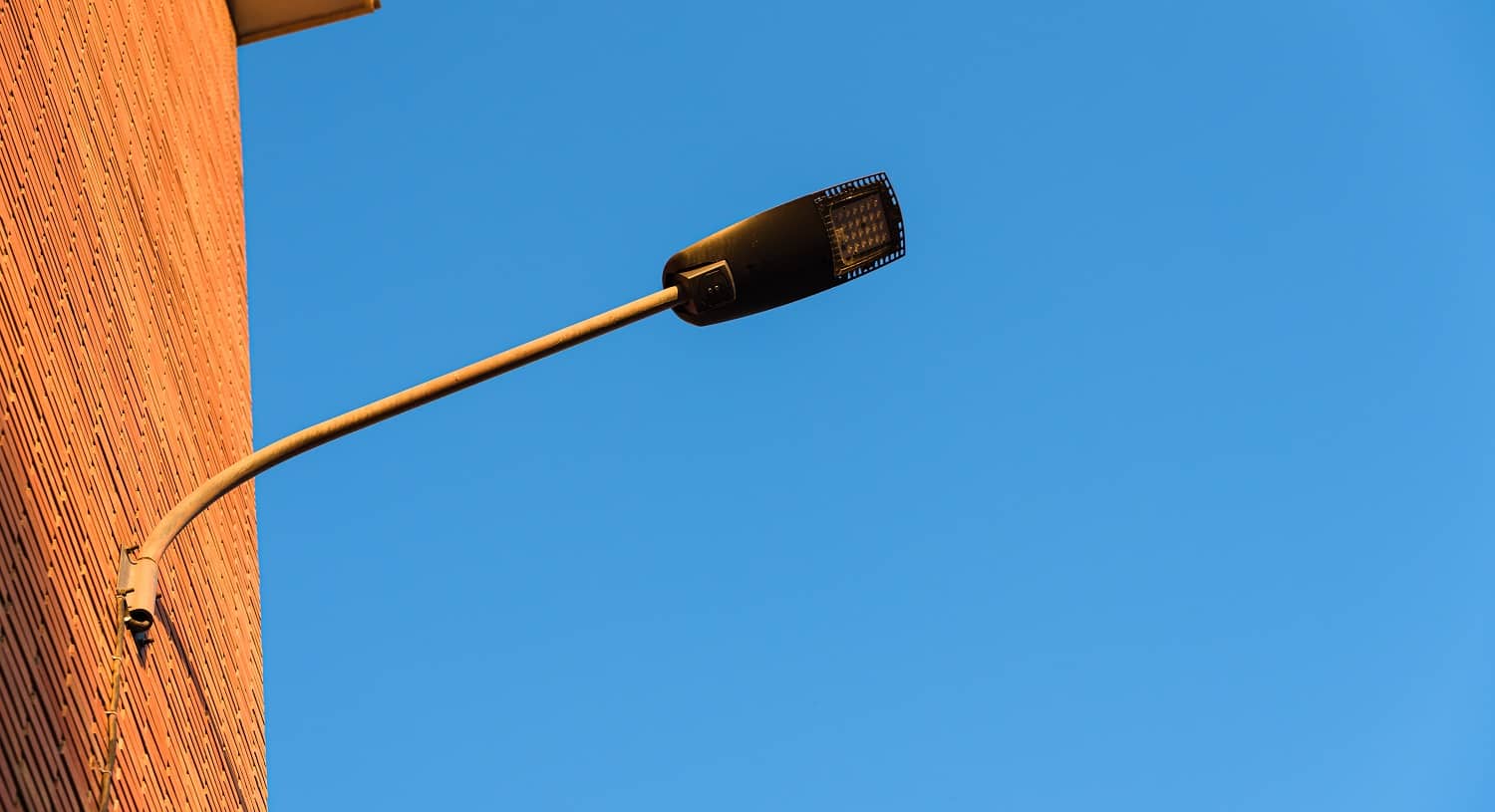Lamppost on the red wall of a building, by day, with a blue sky background.