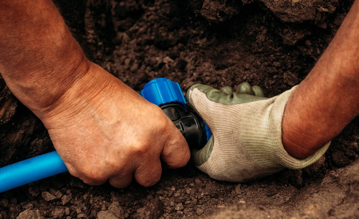 The worker twists the joint in the hose in the garden system in the garden