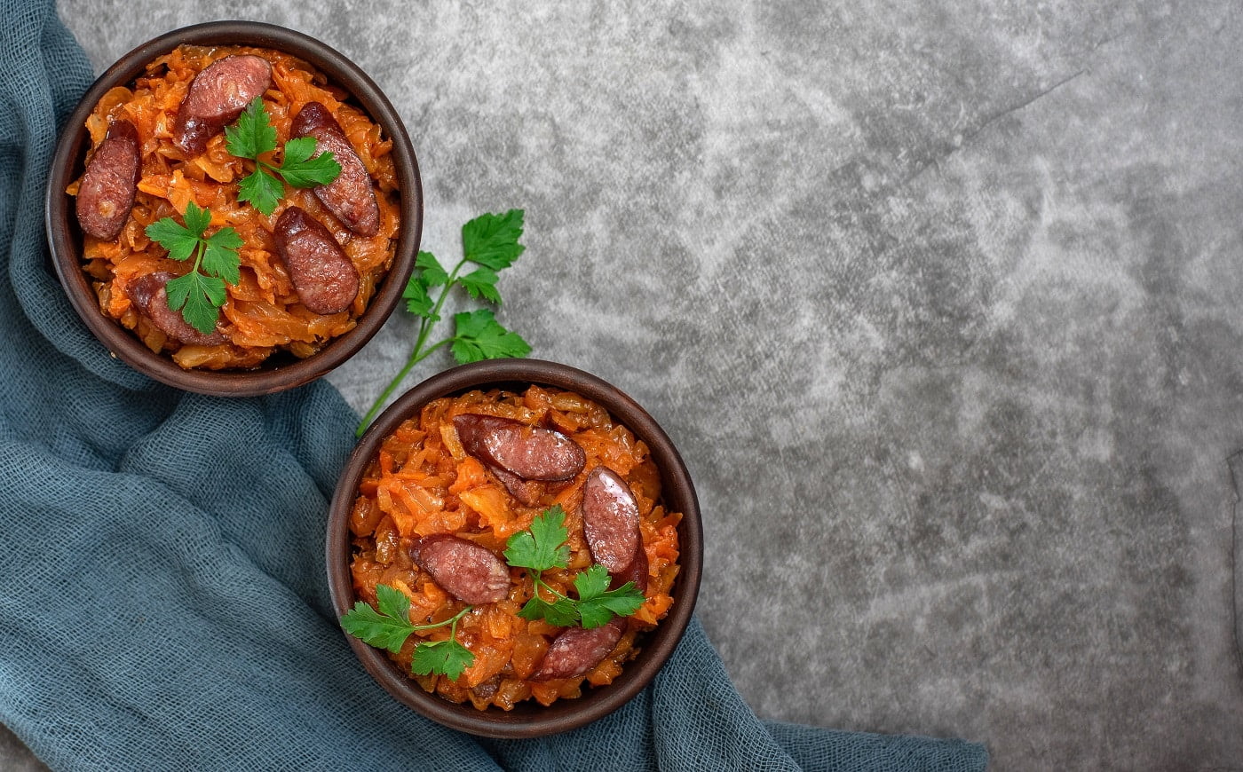 Cabbage stew in bowl with smoked sausages on grey background. Top view, with copy space.