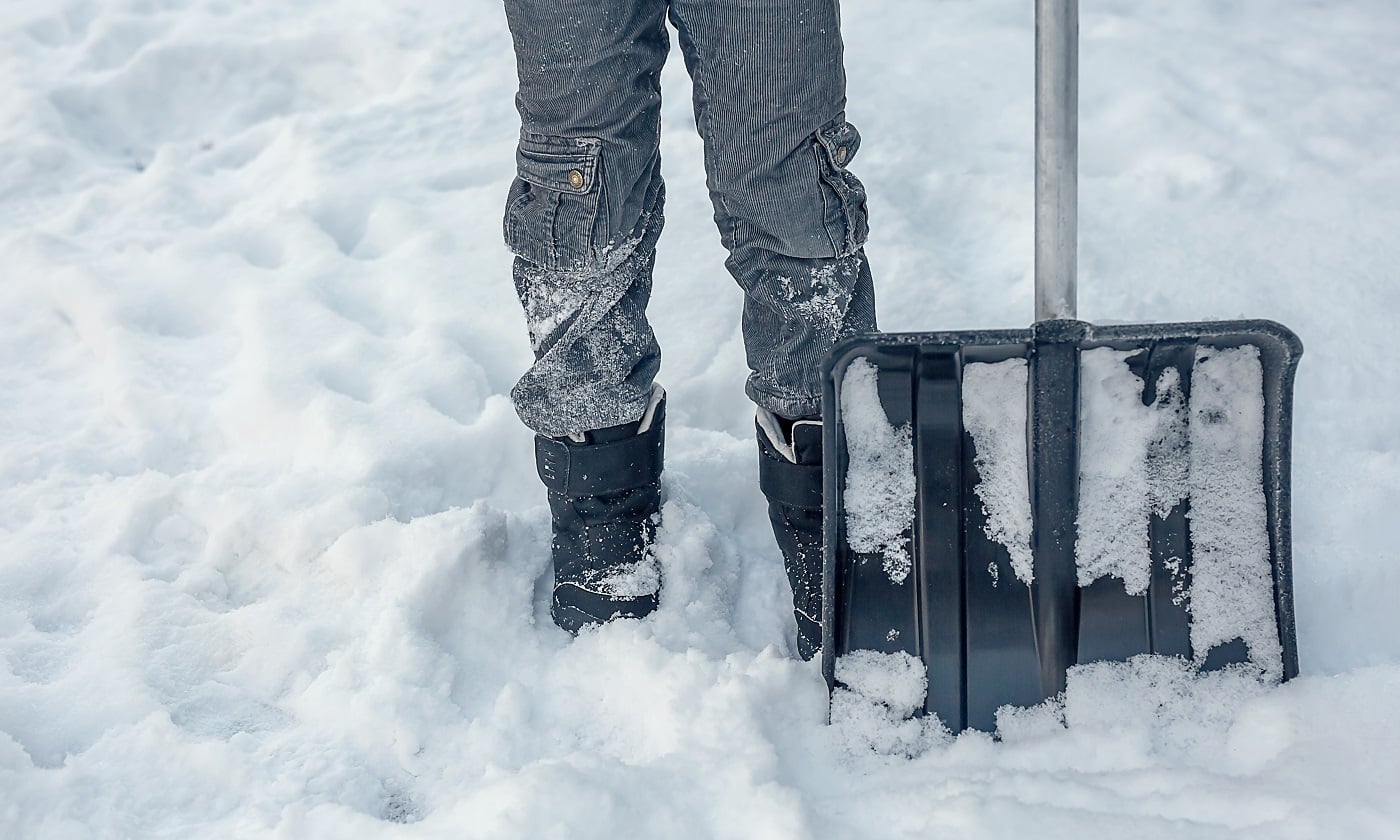 A large snow shovel next to a man in black winter boots.