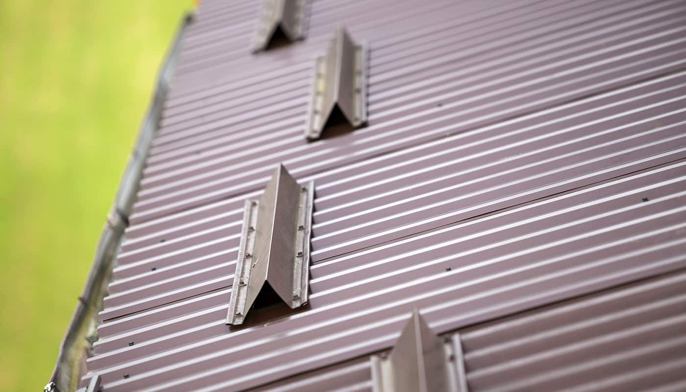 Close-up detail of metal brown shingle tiling house roof surface with rain gutter pipe and snow guards protective fence. Professional work, safety, construction, renovation and durability concept.