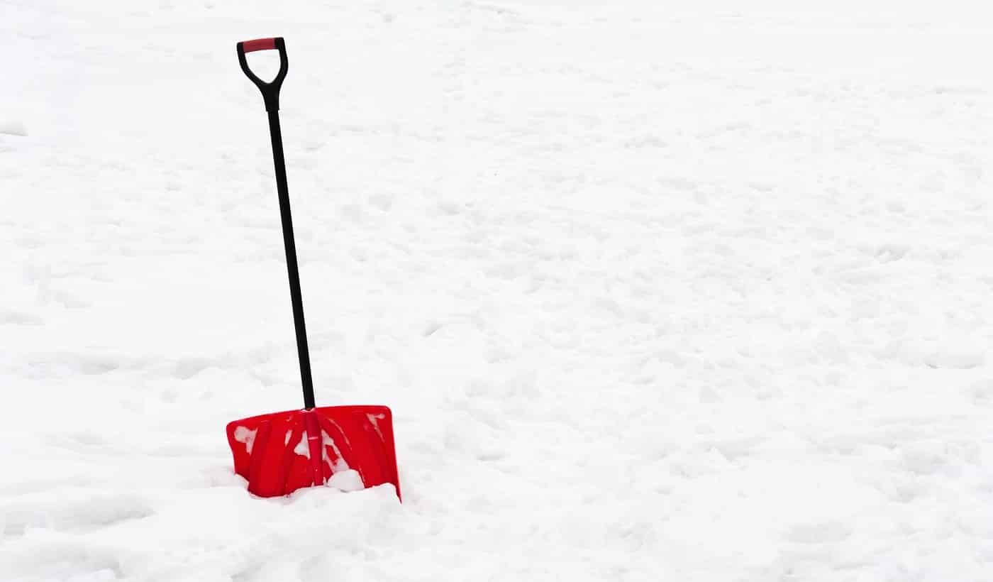Red plastic shovel with black handle stuck in fluffy white snow.