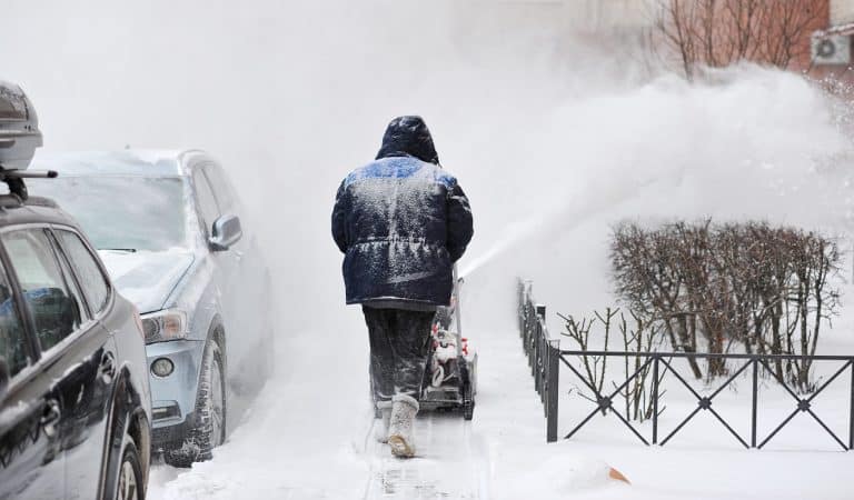 man removes snow in the yard of a multistory building with snow machines