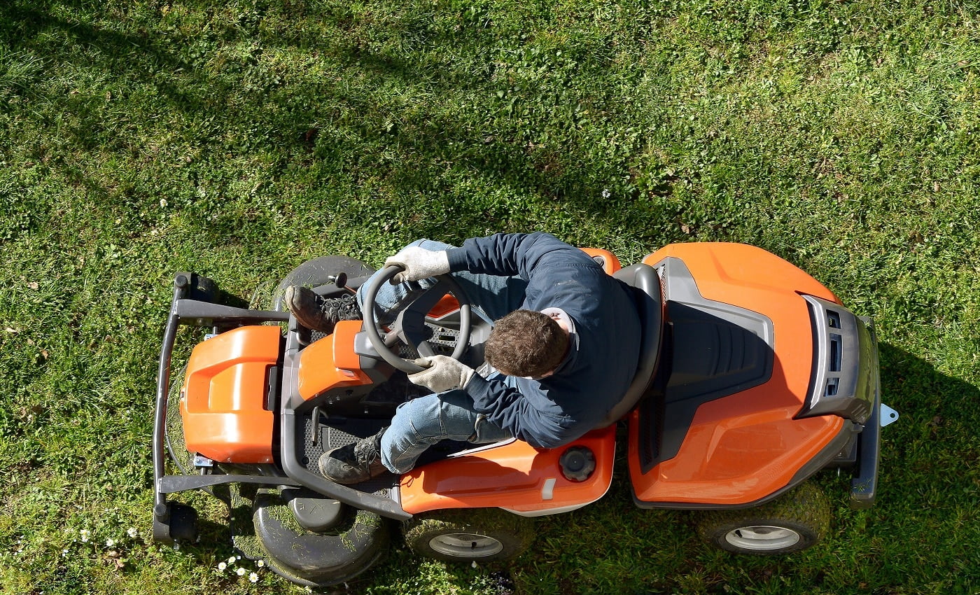 View from above of a man mowing a lawn on an orange ride-on mower as he attends to yard maintenance