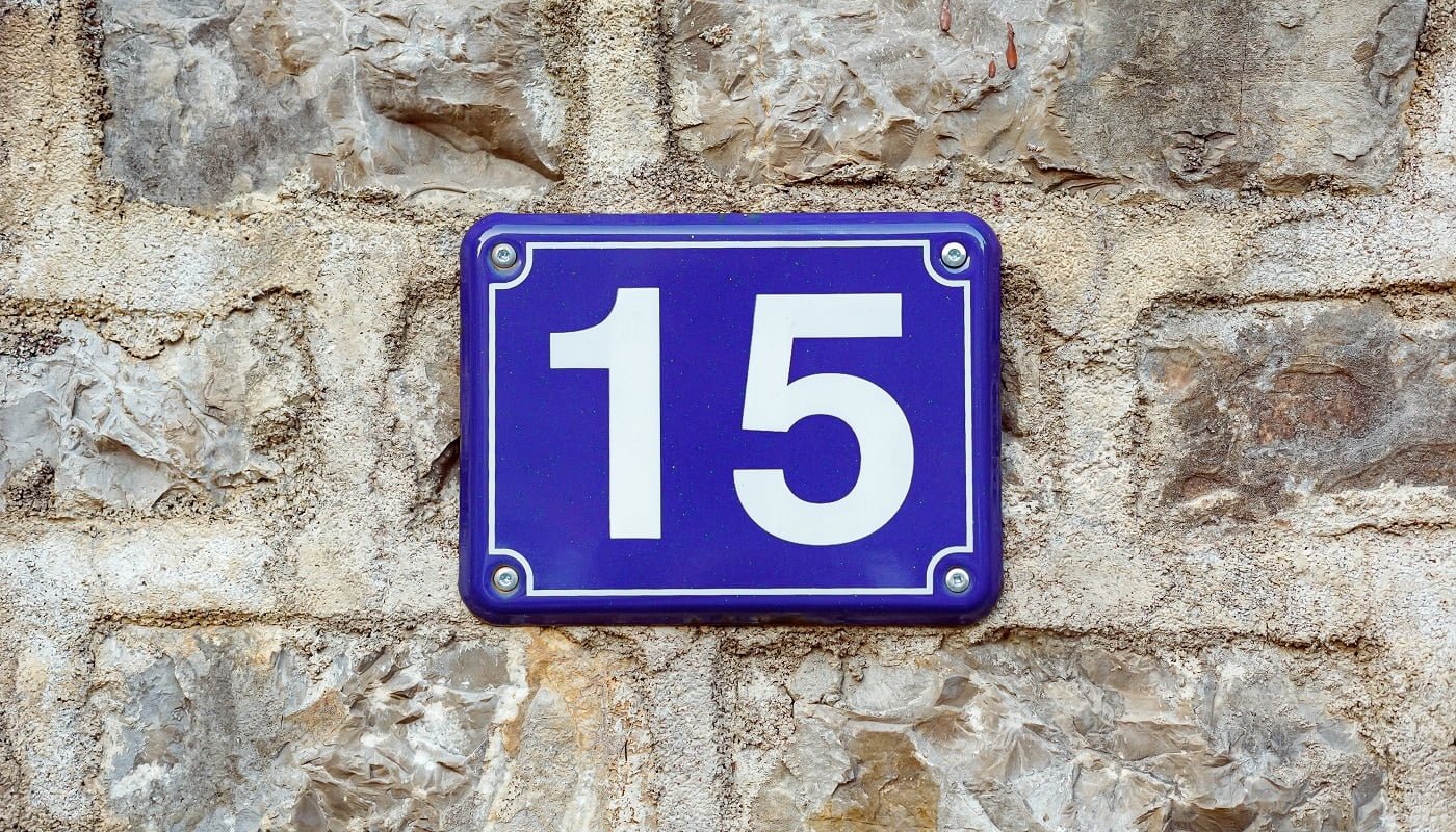 Blue house number fifteen on a stone wall background, closeup
