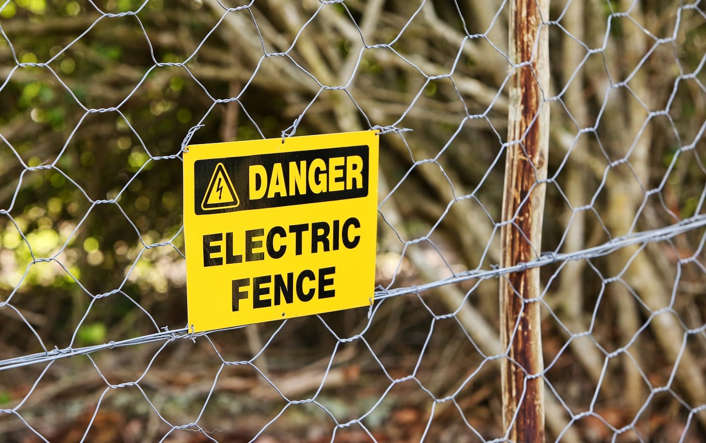 A danger sign hung from the electric fence with the trees in the background
