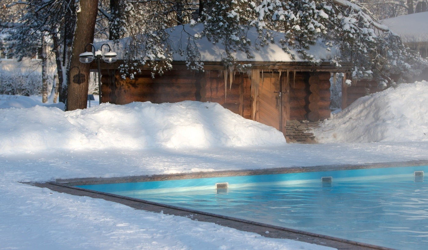 Warm swimming pool with blue water and wooden Russian bath in sunny winter weather, outdoor.