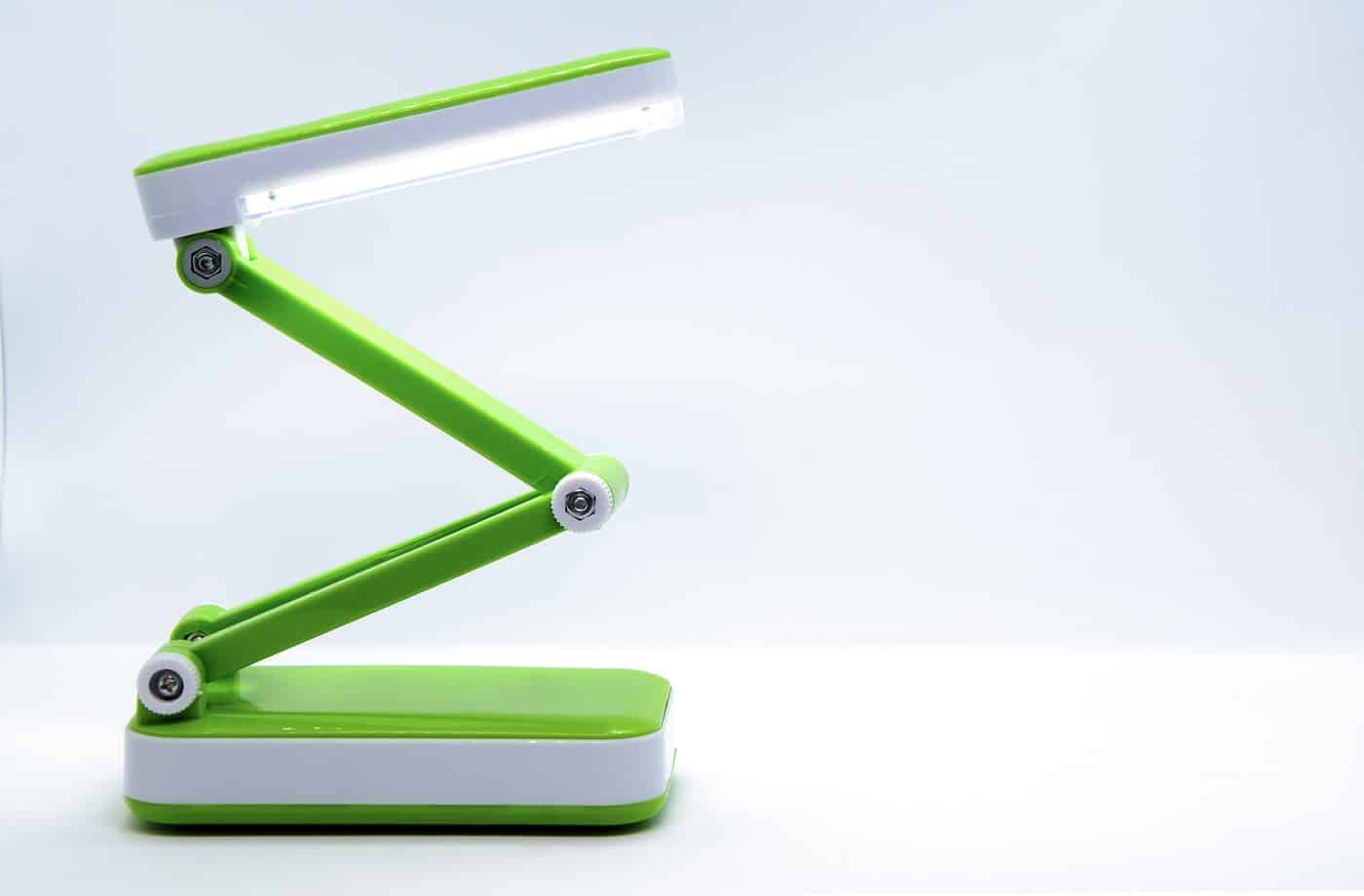 Compact foldable portable LED Desk Lamp with flexible body made of bright green plastic on a white background. Space for text.