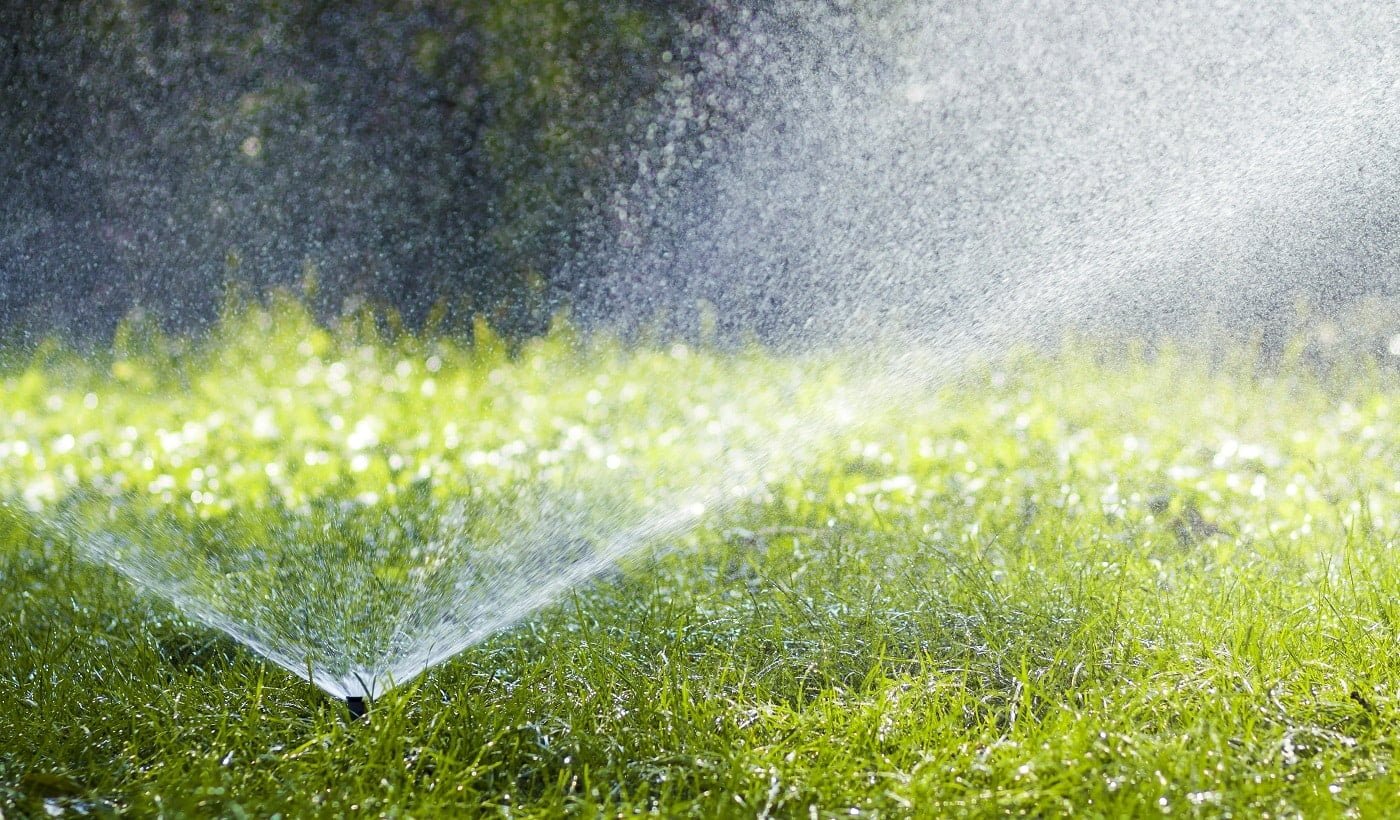 Lawn water sprinkler spraying water over grass in garden on a hot summer day. Automatic watering lawns. Gardening and environment concept.