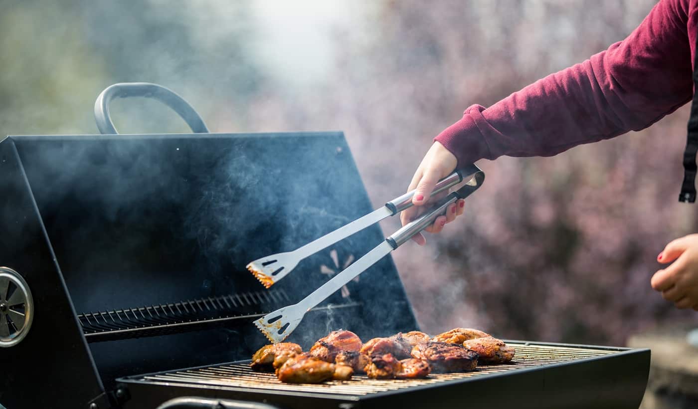 Young woman grills some kind of marinated meat and vegetable on gas grill during summer time