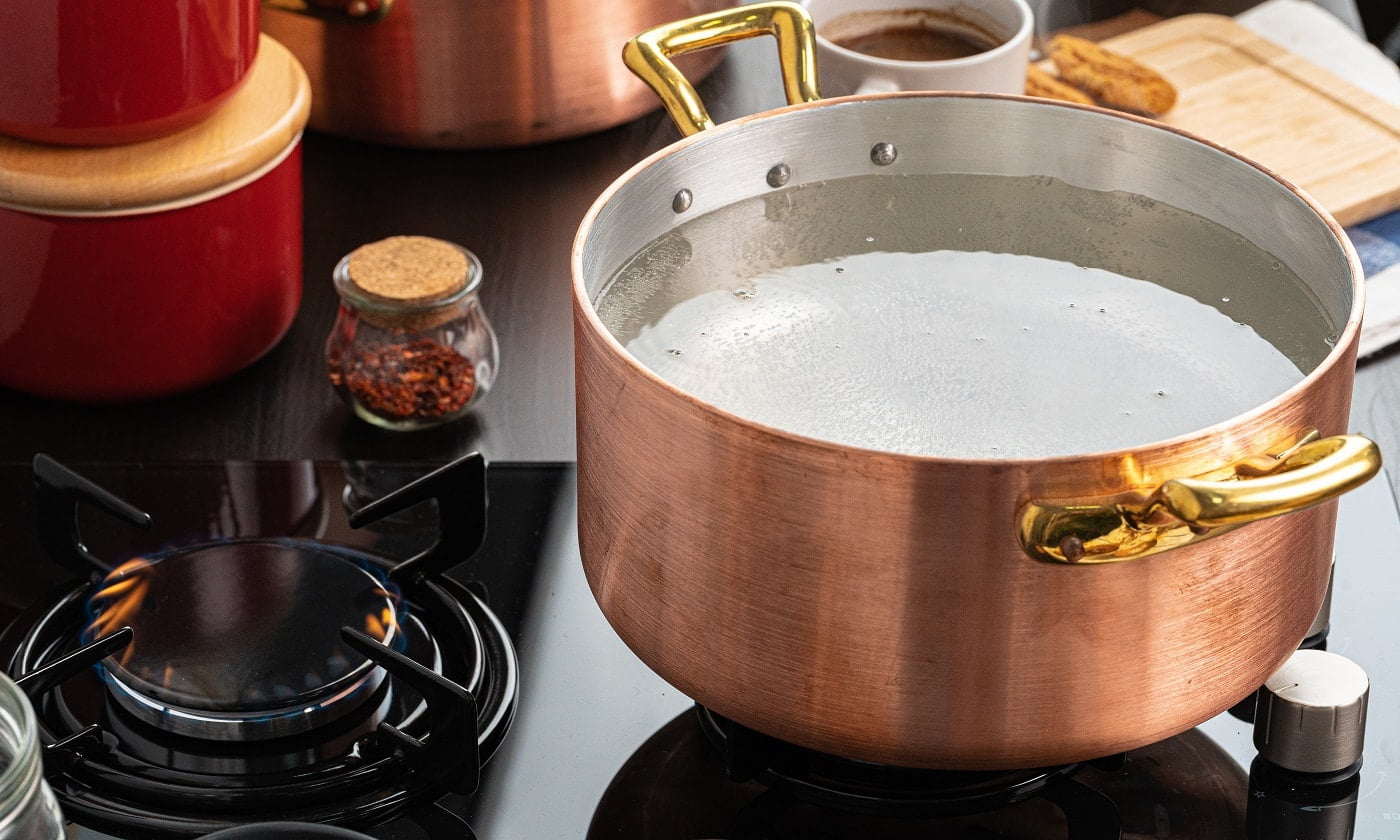 Copper pot with boiling water on a gas stove close up