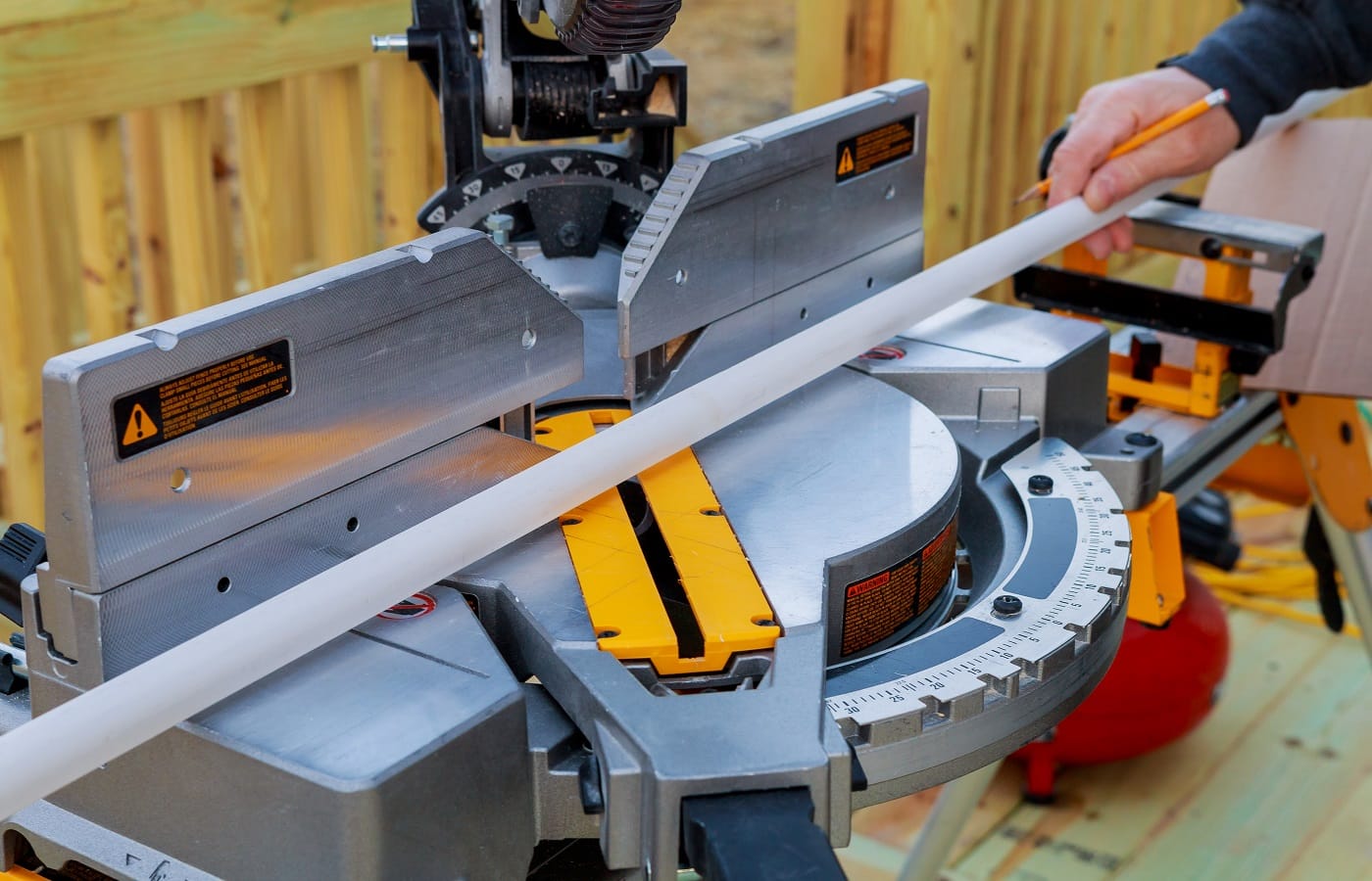 Closeup of mature man sawing lumber with sliding compound miter saw outdoors, sawdust flying around. Top 12-Inch Miter Saw Verdict.