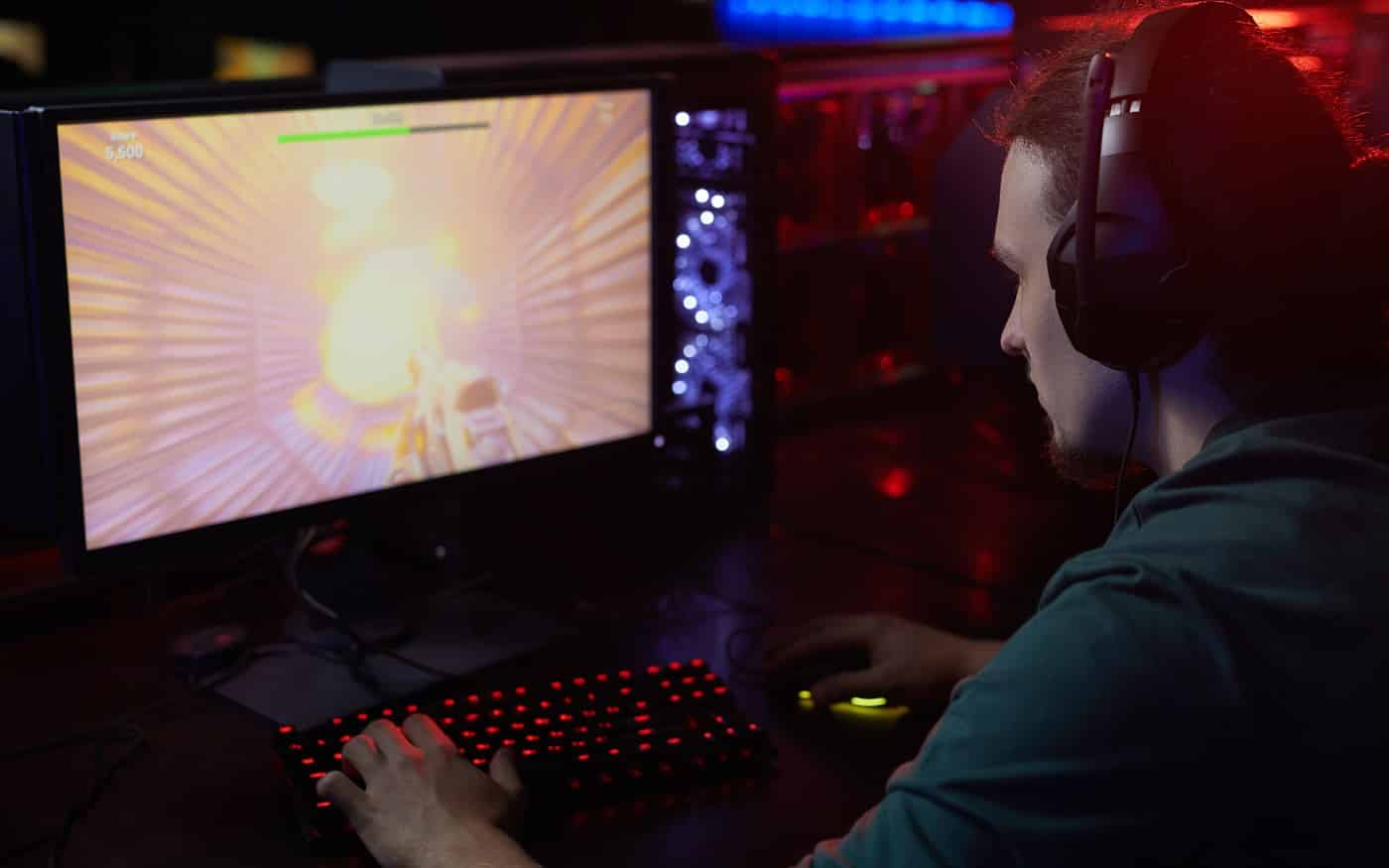 Rear view of young gamer in headphones sitting in front of computer monitor and streaming the computer game