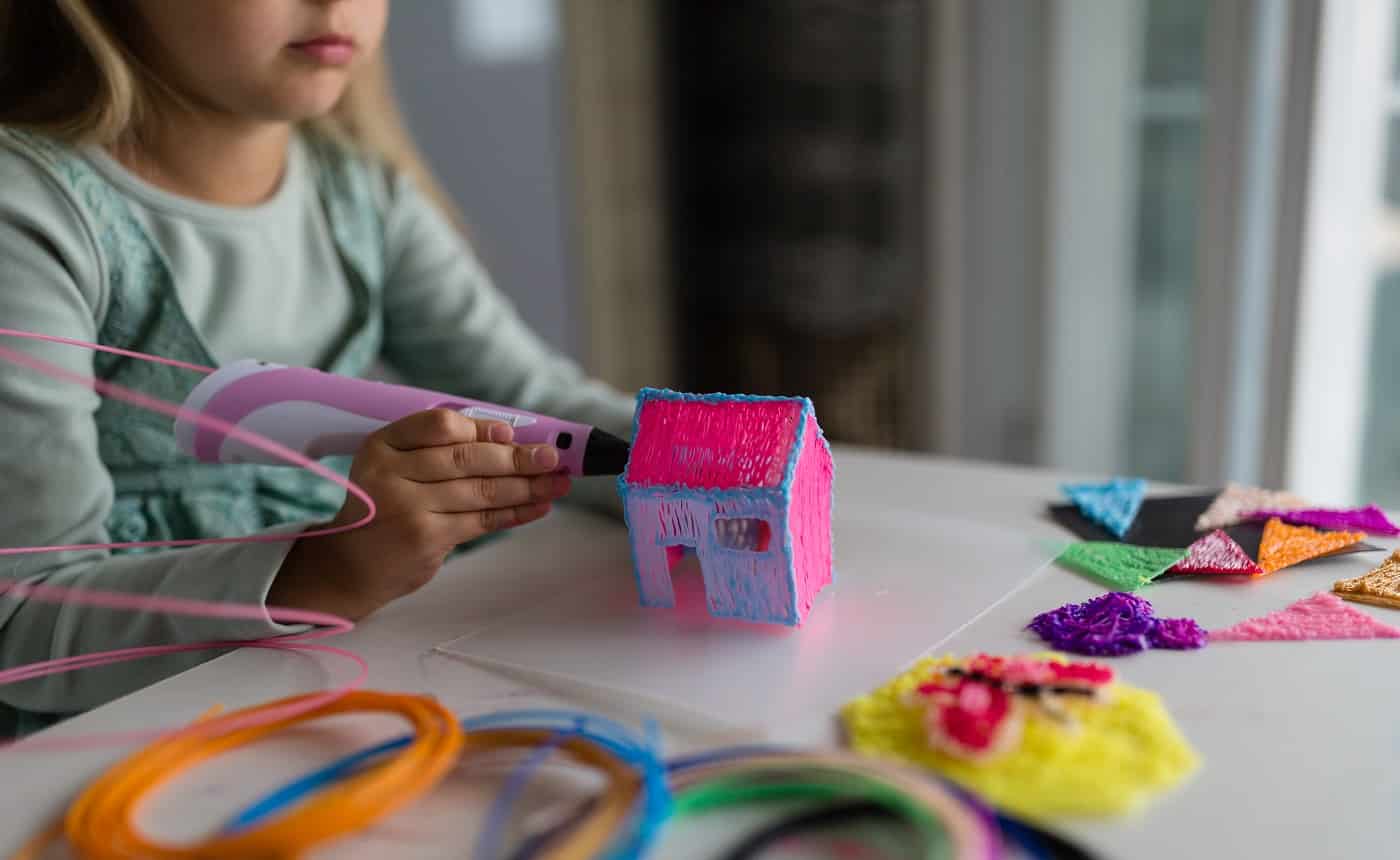 Cute little girl with blonde hair makes a plastic house, draws parts with a 3D pen. Best 3D Pens.STEM and STEAM education. Development, modeling, education, design with hot plastic. Modern technologies. DIY.