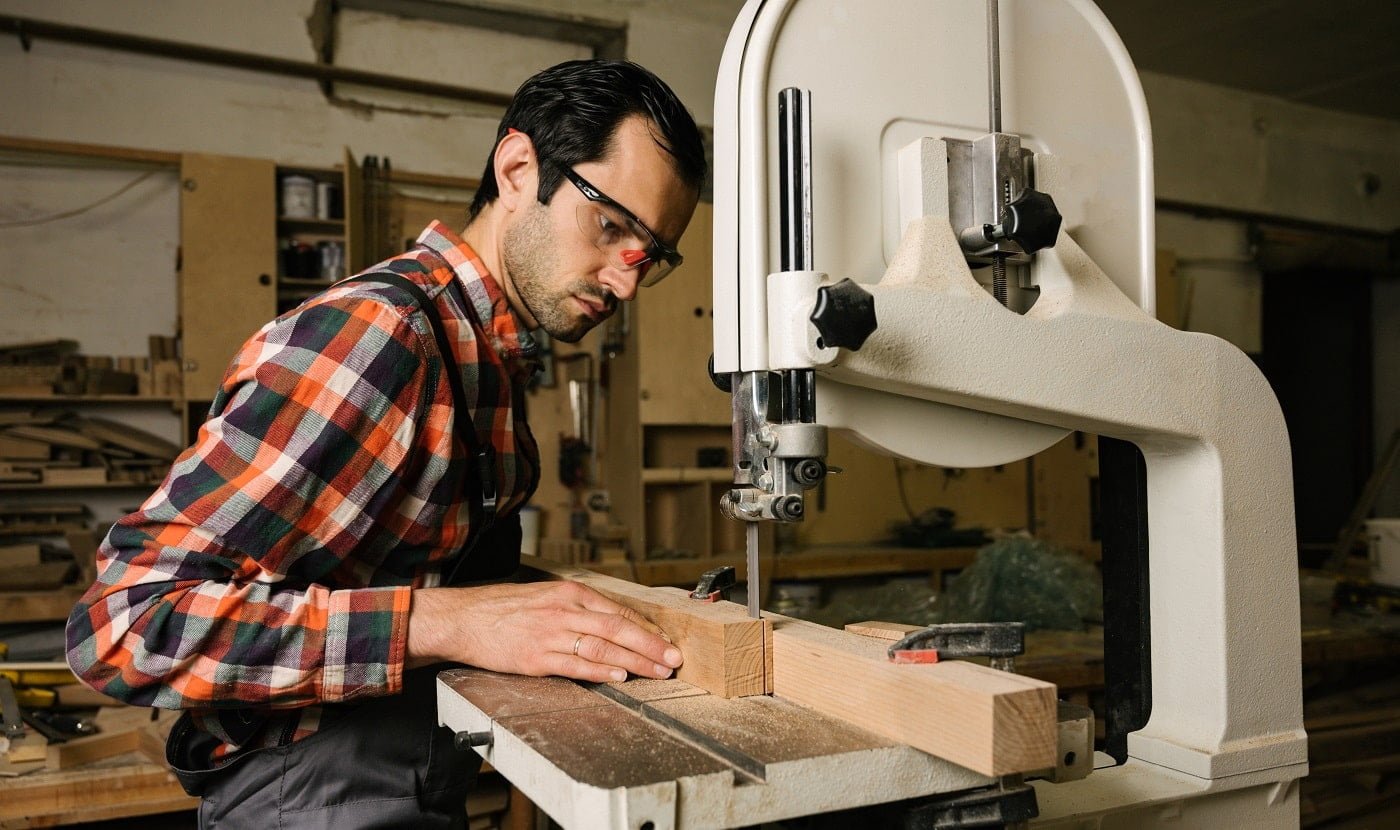 Working process in the carpentry workshop.A man in overalls works on a band saw in a carpentry workshop.Profession, carpentry, woodwork and people concept