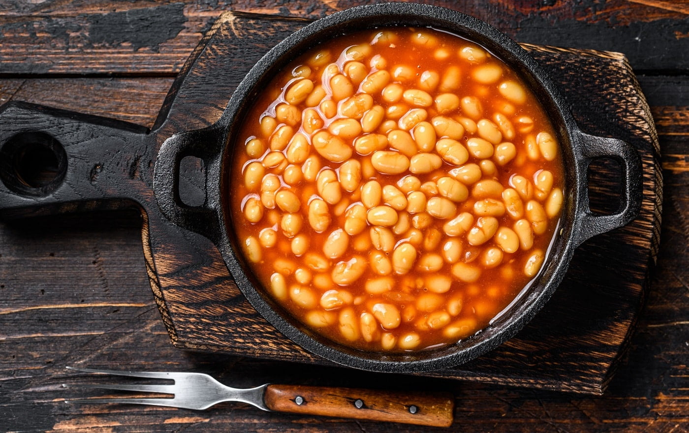 Beans in tomato sauce in a pan. Dark wooden background. top view.