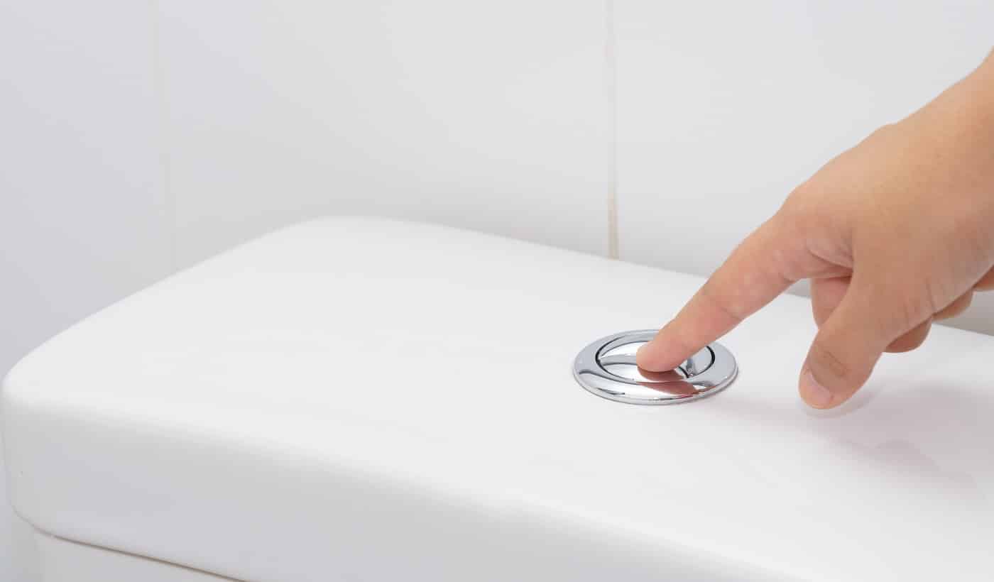 Close up of finger pushing a flush toilet button for cleaning. - save water concept.