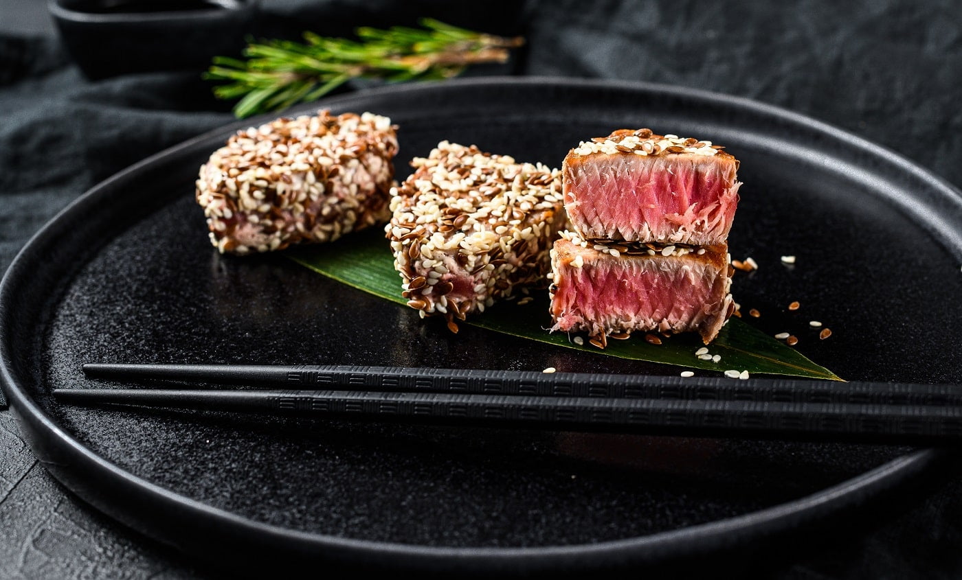 Grilled tuna steak on a plate. Black background. Top view.