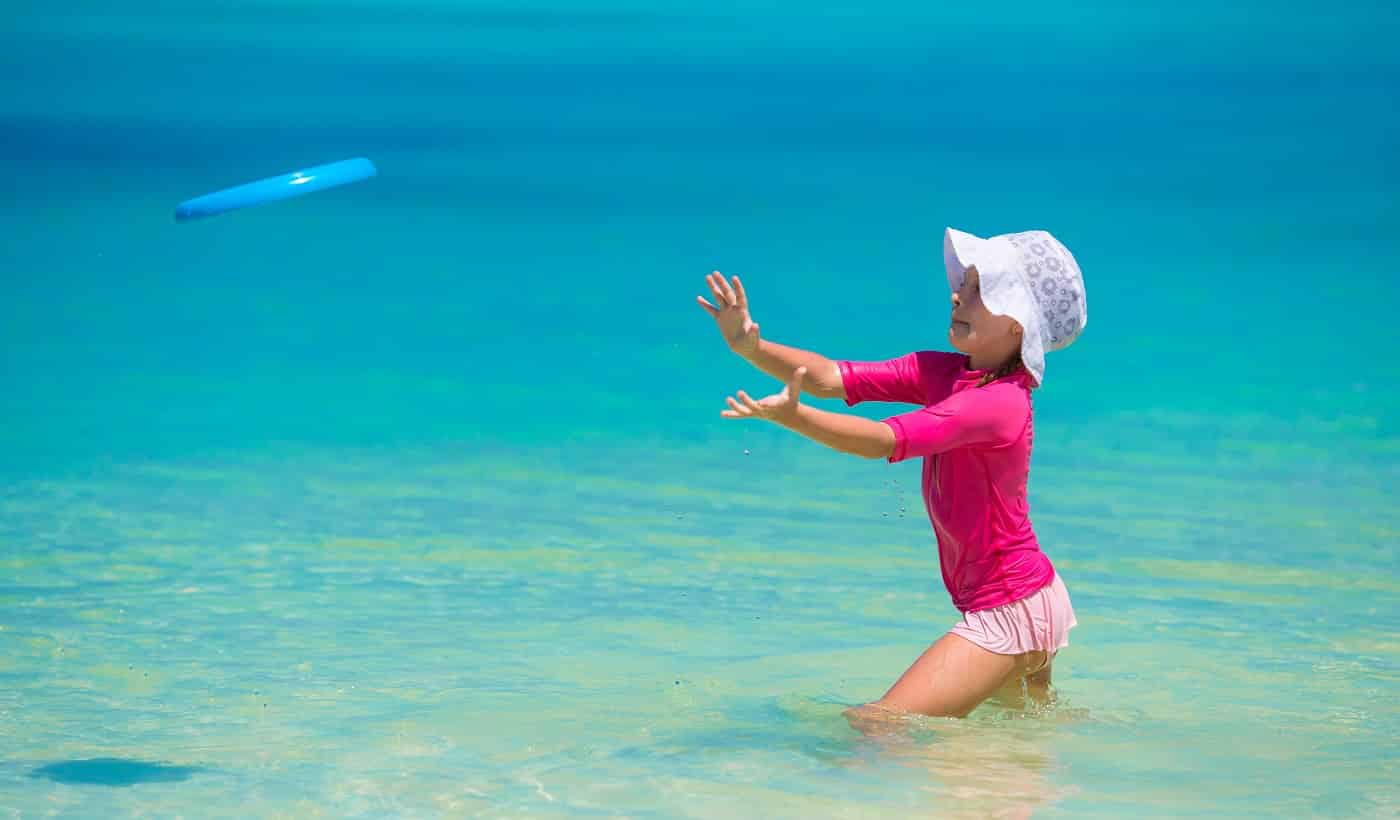 Little girl playing frisbee on a tropical white beach