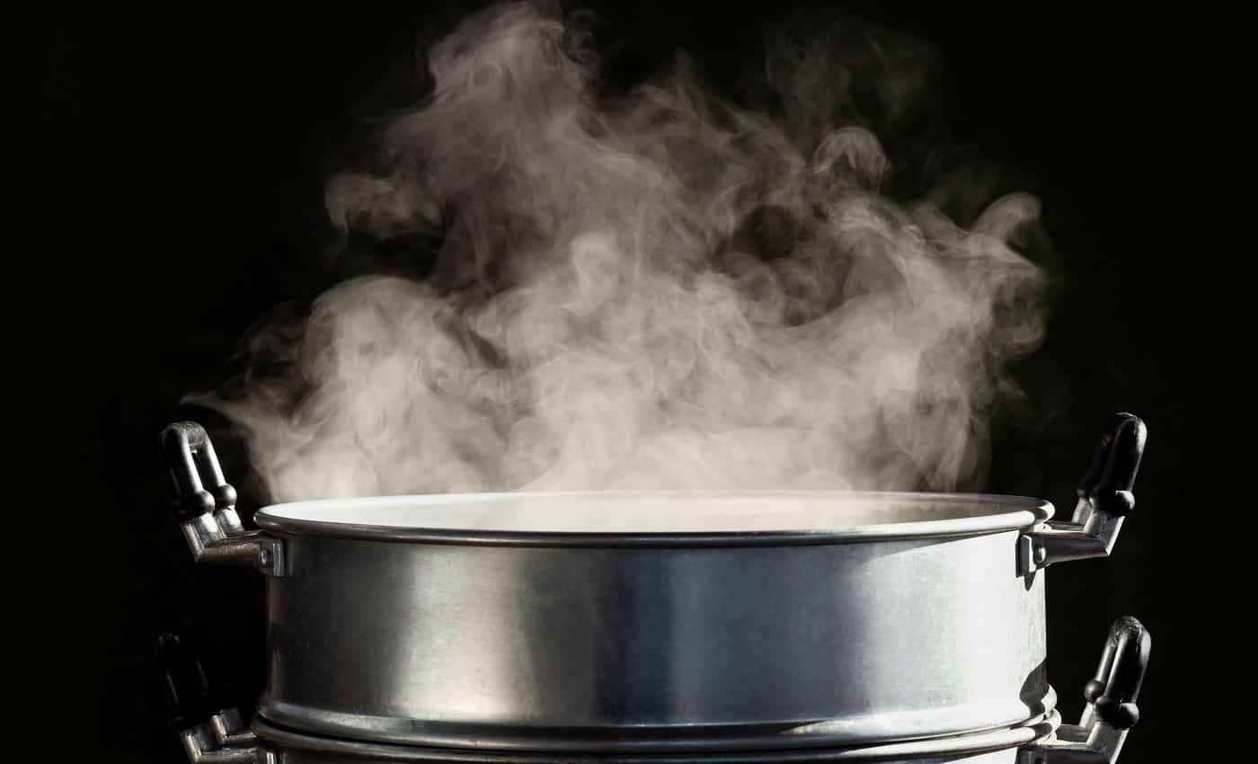 Traditional silver steamer pot with white smoke while cooking on black background