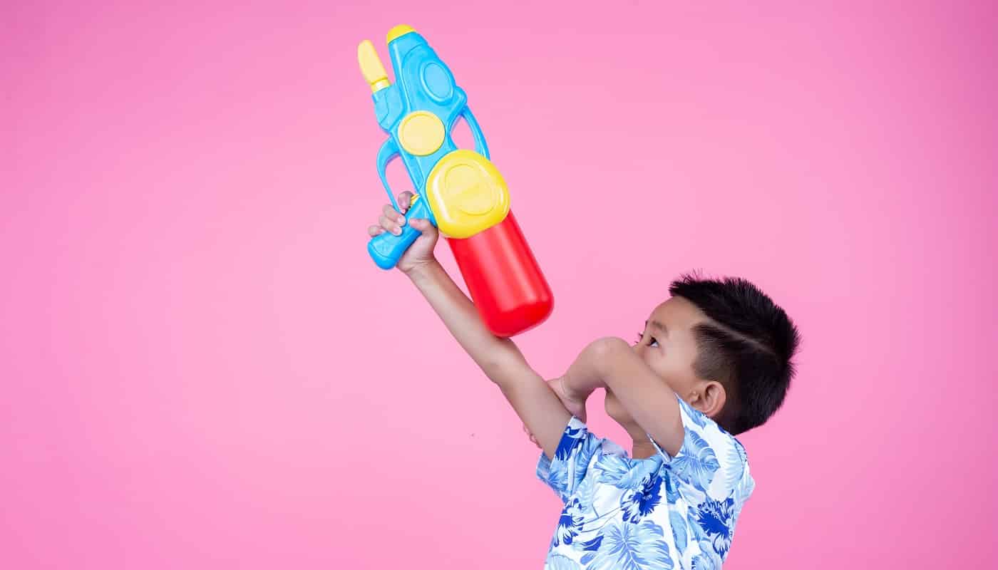 The boy holds a water gun on a pink background.