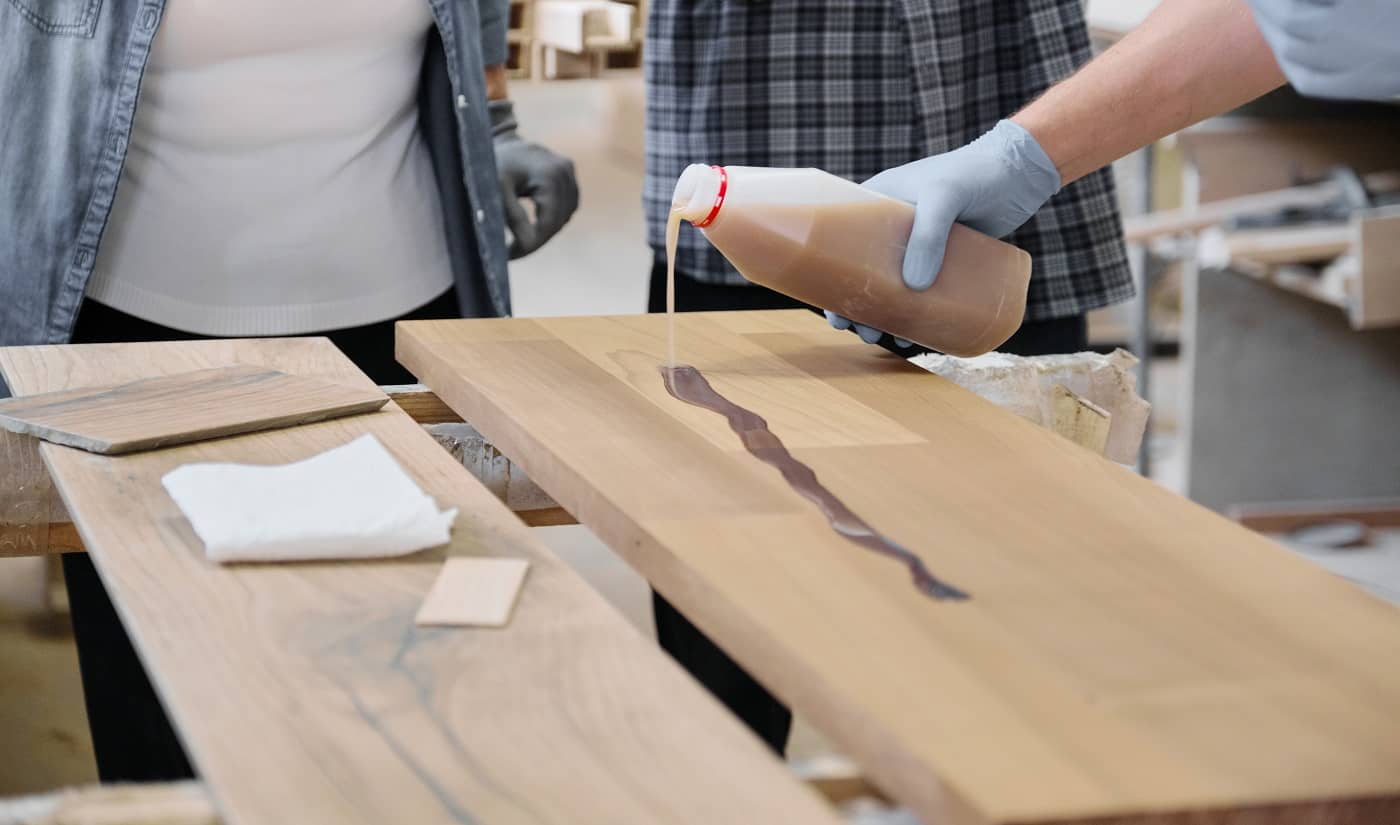 Closeup of worker hand in protective gloves with finishing protective cover for wood, background carpentry furniture woodworking production. Final Words On Food Safe Wood Finish