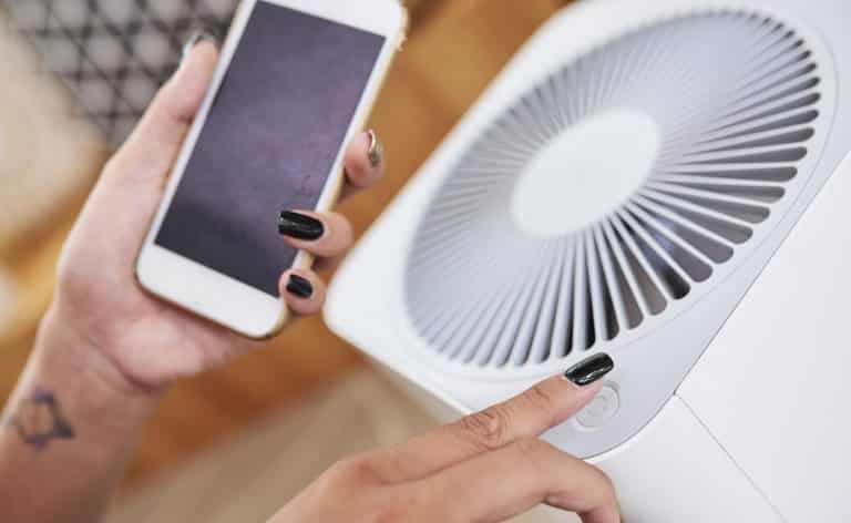 Close-up image of woman turning on air conditioner and using smart home application on her phone to manage temperature