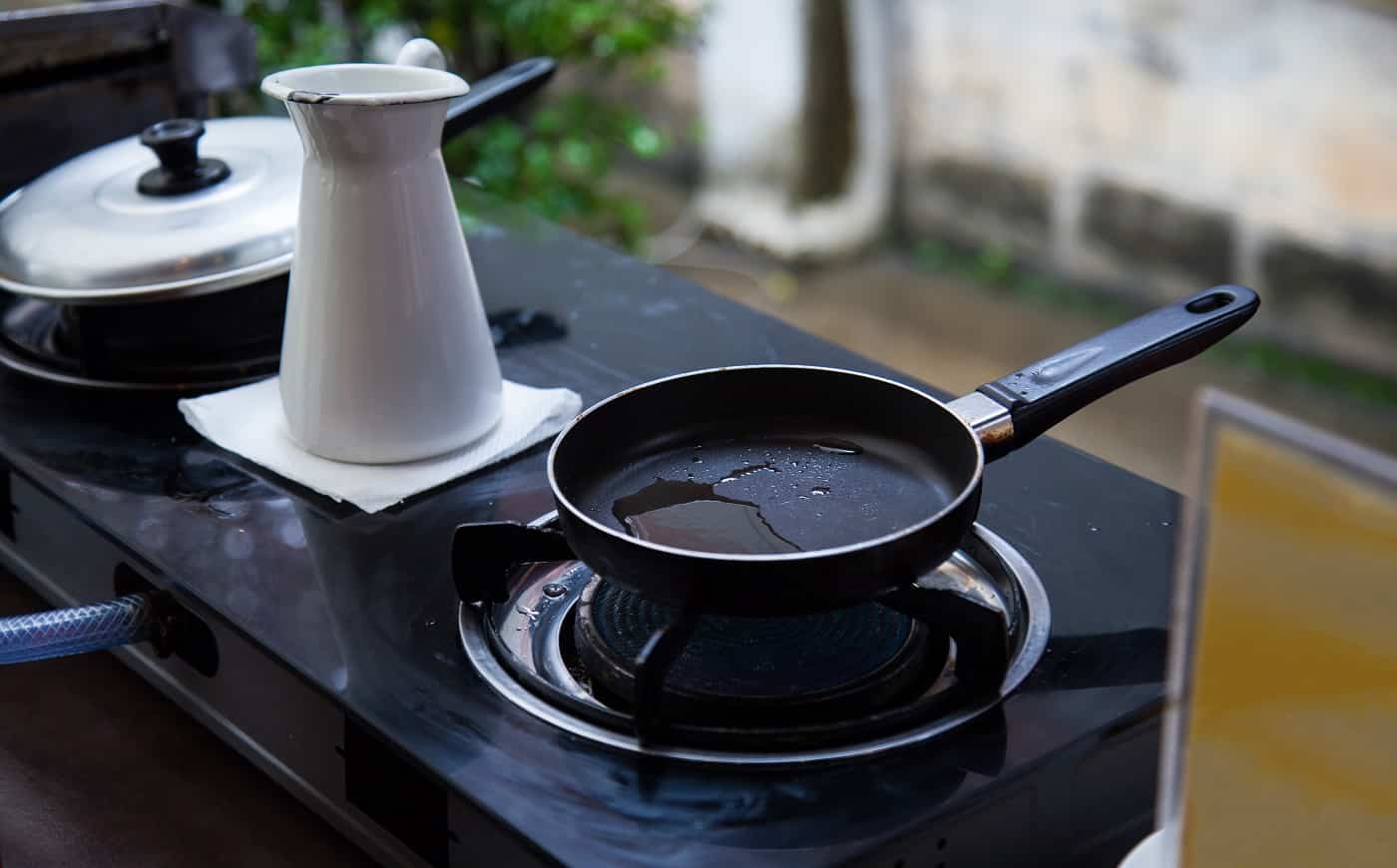 heating oil in stainless steel pan on gas fueled stove, prepared for frying breakfast or lunch food in an outdoor kitchen background. Kitchen Utensils, tools and equipment design concept.