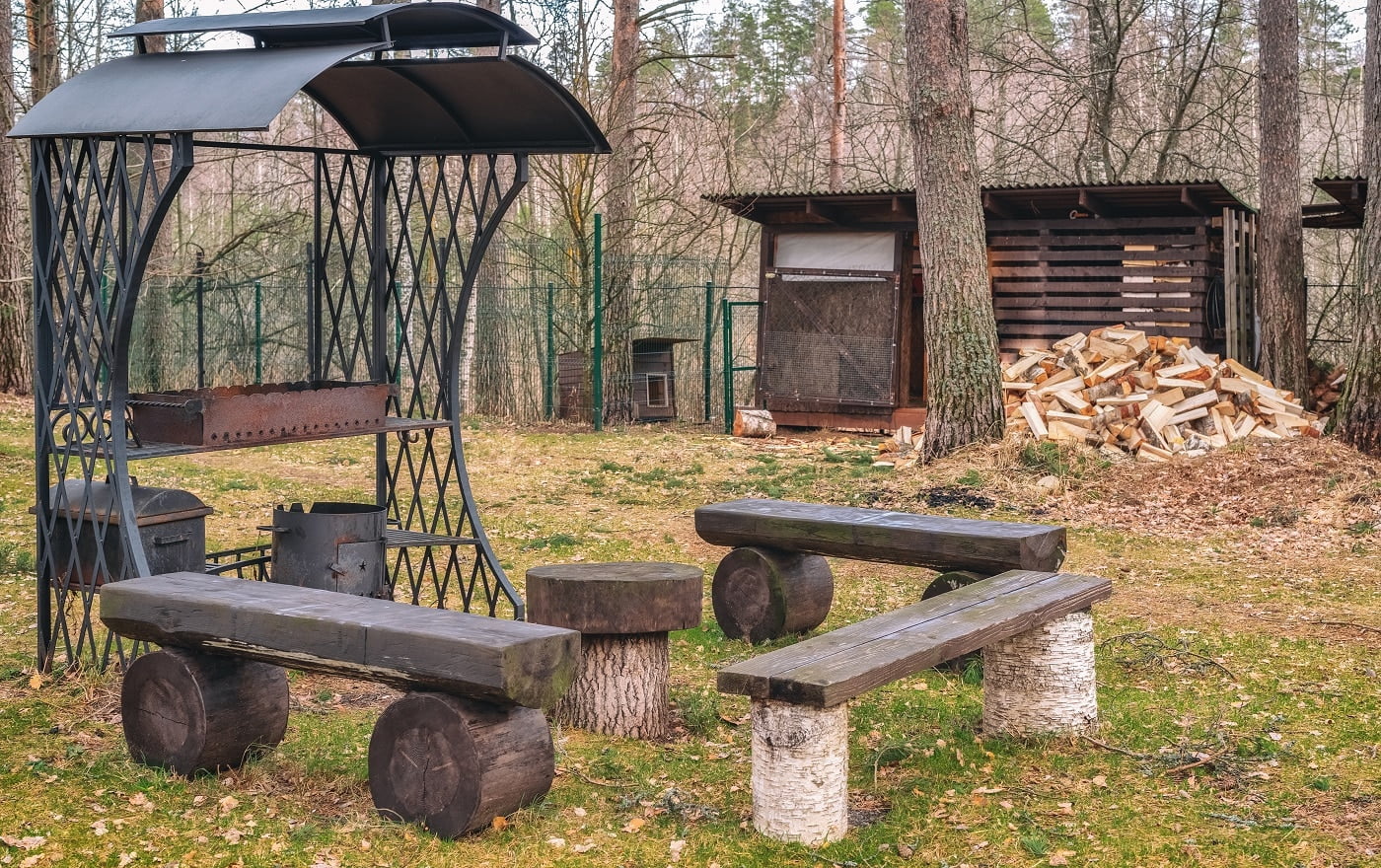 Antique metal brazier made of wrought iron with a beautiful pattern on the background of wood and trees. Table and benches made of logs. Legendary Camp Chef Explorer 2 Stove Verdict