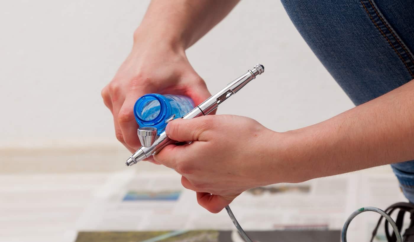 Close-up of a woman artist in jeans cleans and prepares the airbrush for the work of painting the walls.
