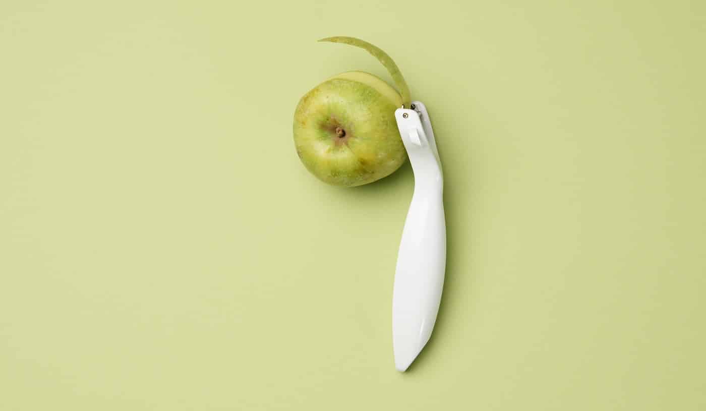 plastic knife for peeling vegetables, fruits and a green apple on a green background, top view