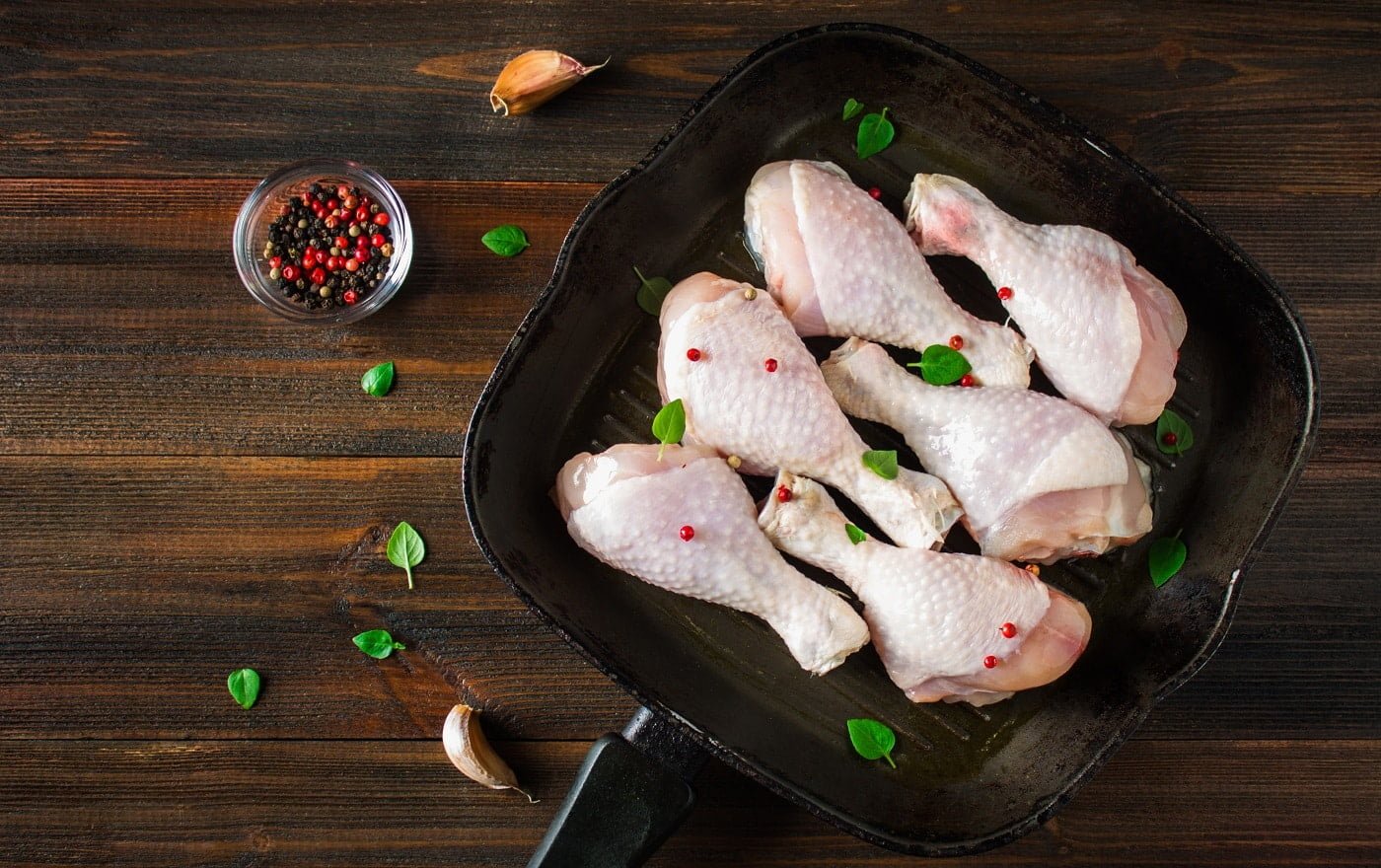 Raw chicken legs in a frying pan on a wooden table. Meat ingredients for cooking. Top view. Closeup.